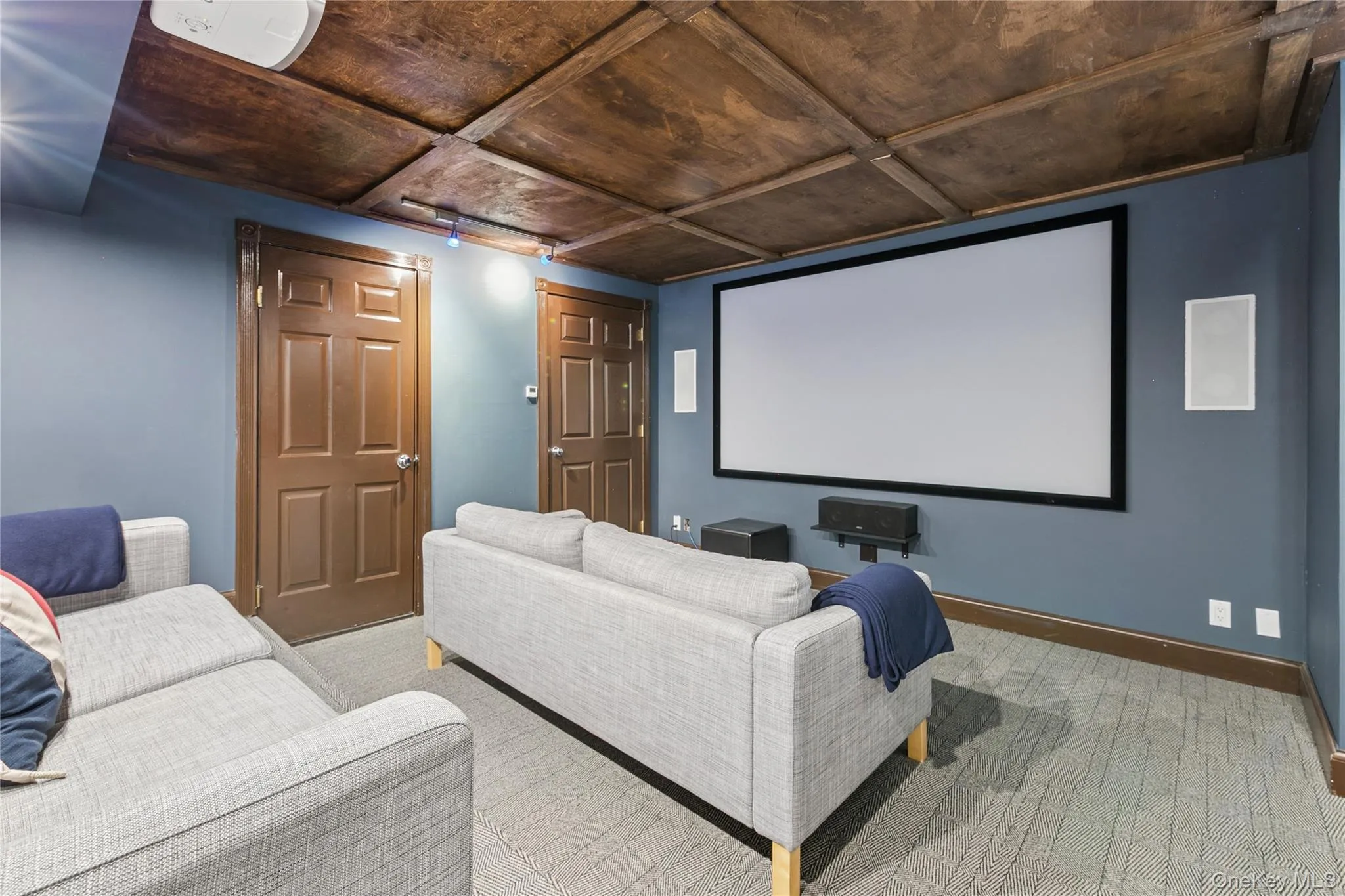 Media room featuring a large projection screen, two in-wall speakers, wood-paneled ceiling, and a patterned carpet Media room featuring a large projection screen, two in-wall speakers, wood-paneled ceiling, and a patterned carpet