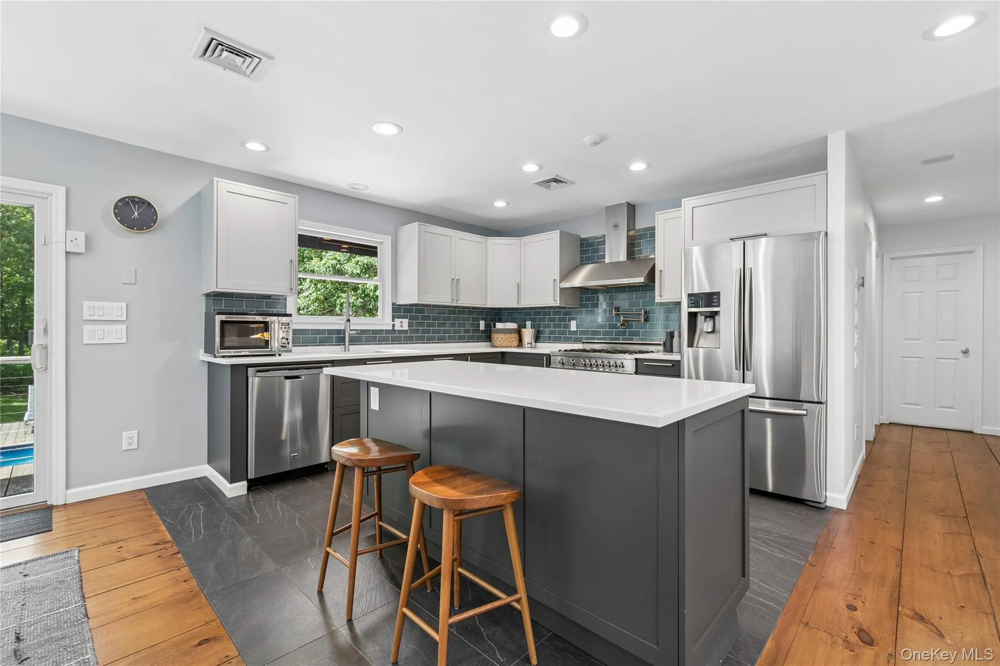 Kitchen featuring a central island with white countertop, two-tone cabinetry, stainless steel appliances, a tile backsplash, and recessed lighting Kitchen featuring a central island with white countertop, two-tone cabinetry, stainless steel appliances, a tile backsplash, and recessed lighting