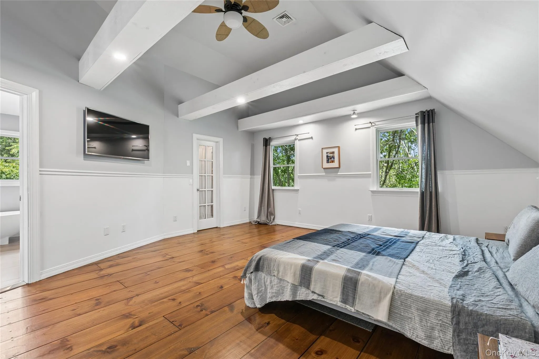 Vaulted ceiling with exposed white beams and a ceiling fan, complemented by warm wood-finish flooring Vaulted ceiling with exposed white beams and a ceiling fan, complemented by warm wood-finish flooring