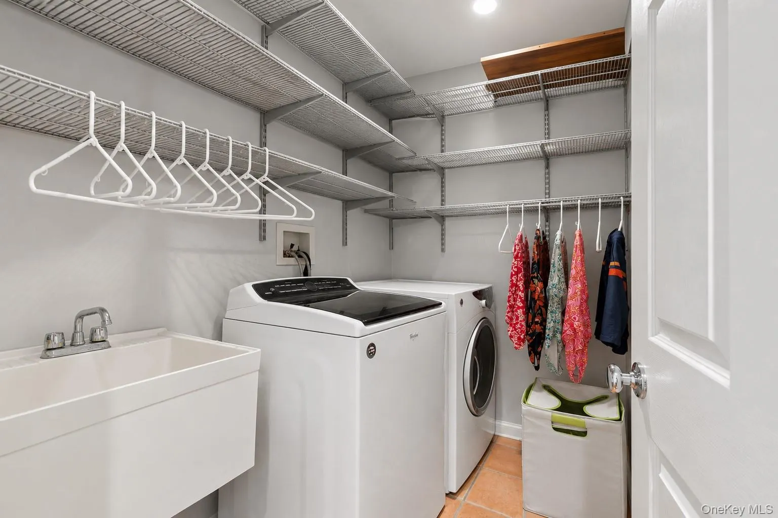 Dedicated laundry room featuring a utility sink, extensive wire shelving, a hanging rod, and tile flooring Dedicated laundry room featuring a utility sink, extensive wire shelving, a hanging rod, and tile flooring
