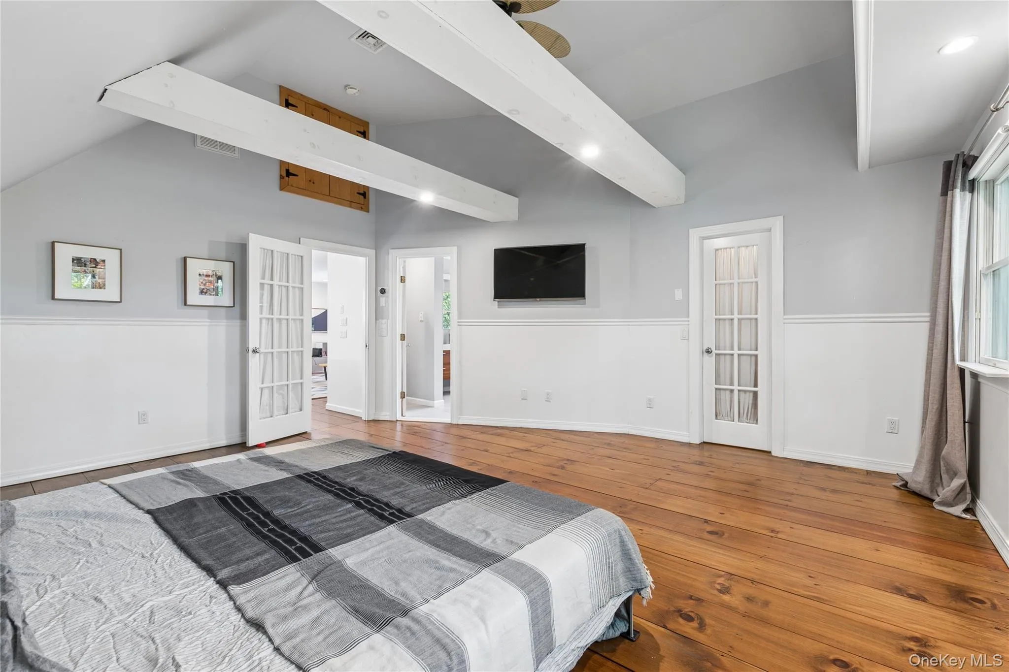 Spacious room featuring exposed ceiling beams, wood-finish flooring, vaulted ceilings, and wainscoting Spacious room featuring exposed ceiling beams, wood-finish flooring, vaulted ceilings, and wainscoting