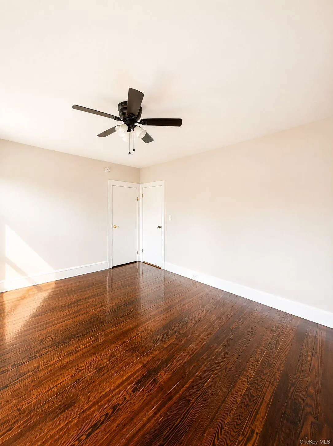 Spacious room with dark wood-finish flooring, multiple windows, and a ceiling fan with integrated lighting Spacious room with dark wood-finish flooring, multiple windows, and a ceiling fan with integrated lighting