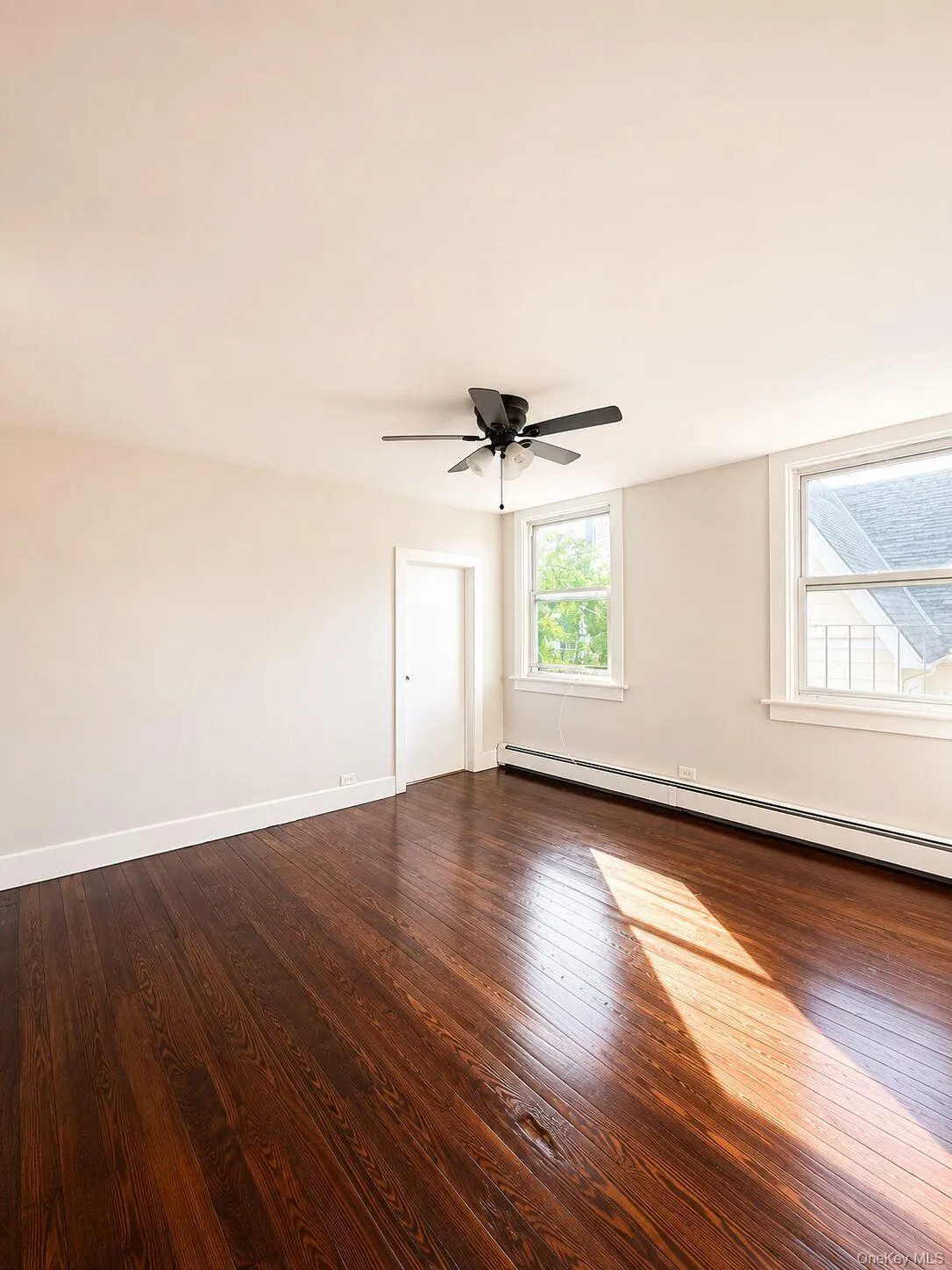 Spacious room featuring dark wood-finish flooring, white baseboards, and light neutral walls Spacious room featuring dark wood-finish flooring, white baseboards, and light neutral walls