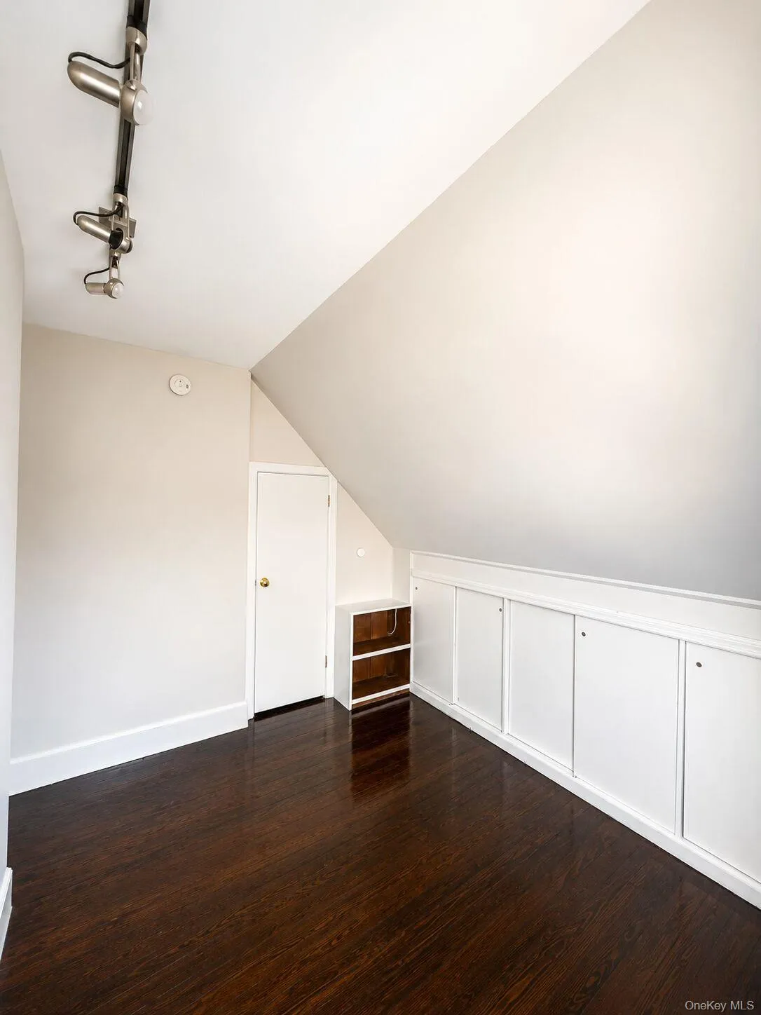 Second bedroom featuring wood-finish flooring, track lighting, and a white paneled storage unit built into the sloped wall Second bedroom featuring wood-finish flooring, track lighting, and a white paneled storage unit built into the sloped wall