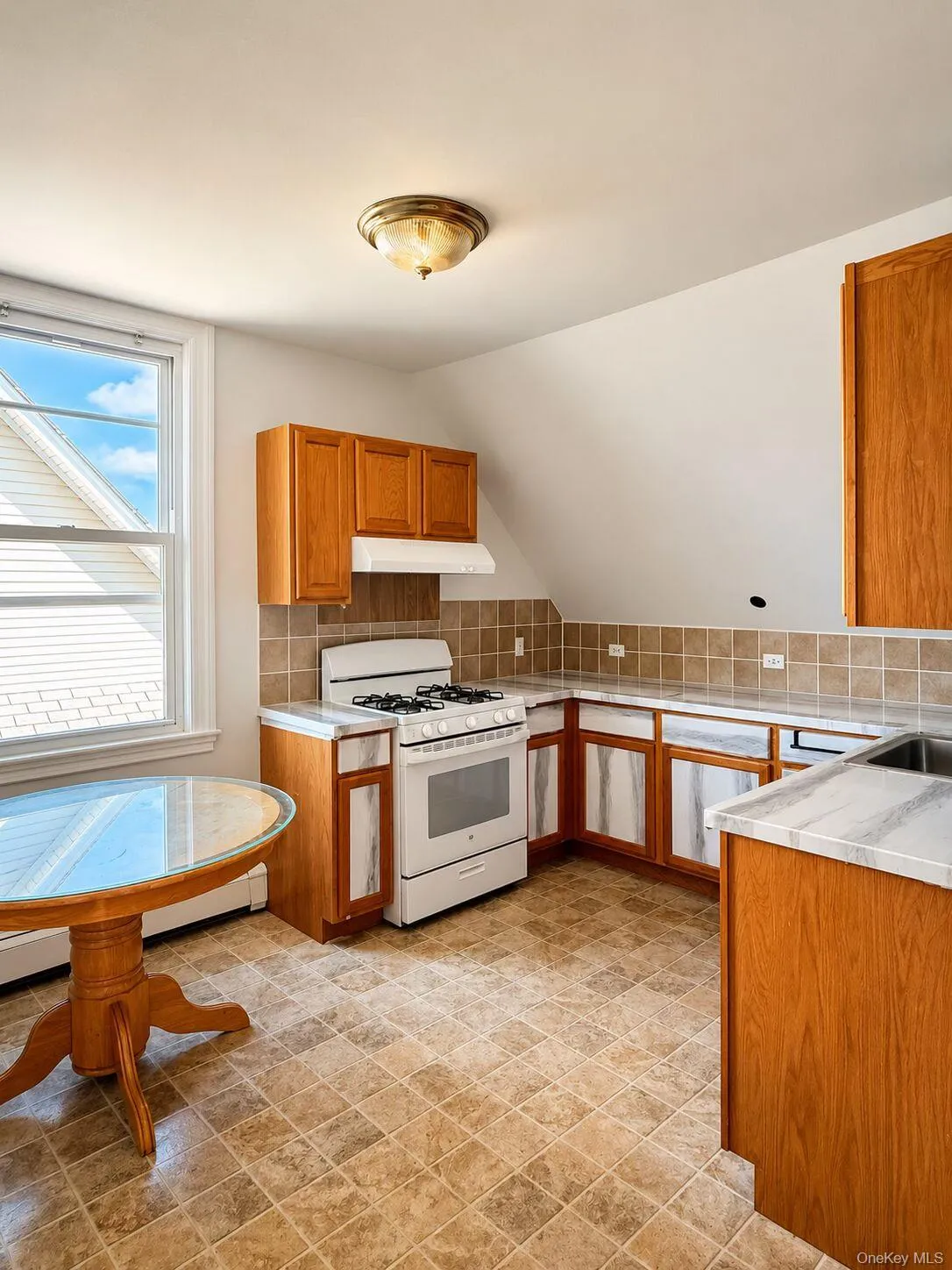 Kitchen featuring light wood cabinetry, white countertops, tile backsplash, and a gas range Kitchen featuring light wood cabinetry, white countertops, tile backsplash, and a gas range