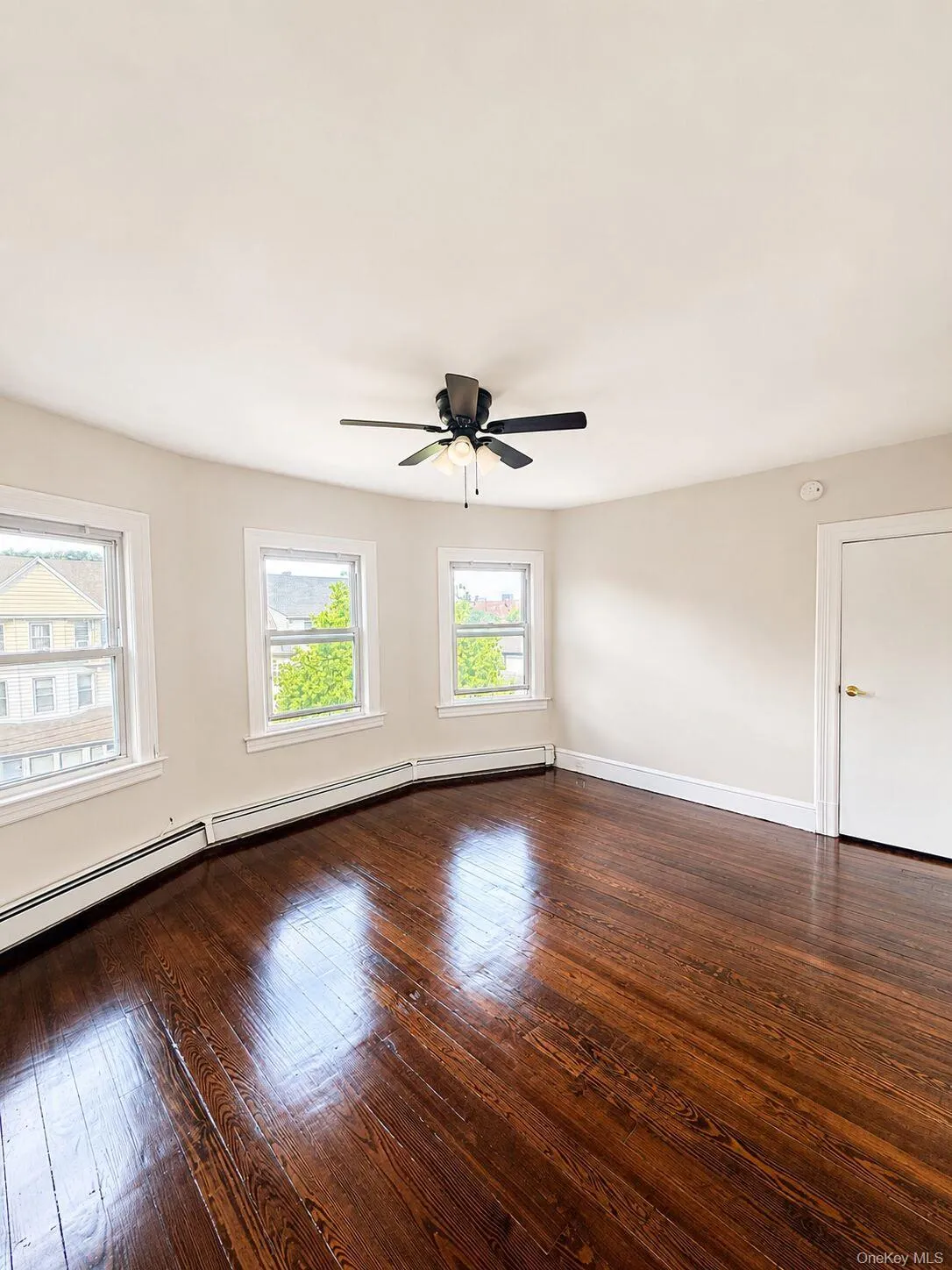 Spacious room with dark wood-finish flooring, multiple windows, and a ceiling fan with integrated lighting Spacious room with dark wood-finish flooring, multiple windows, and a ceiling fan with integrated lighting