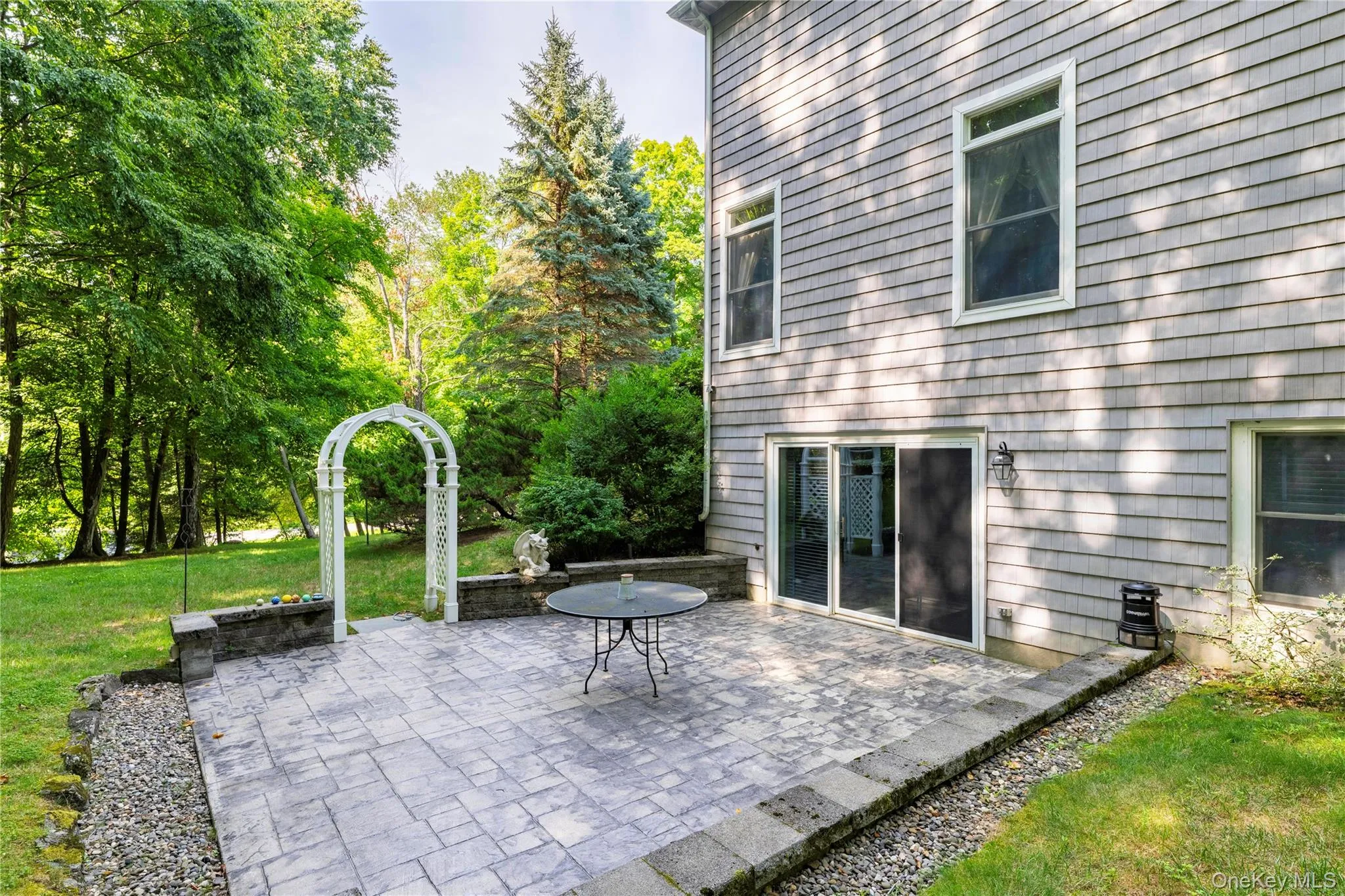 Stamped concrete patio featuring a white lattice arbor, stone planter, sliding glass door access, and exterior wall sconce Stamped concrete patio featuring a white lattice arbor, stone planter, sliding glass door access, and exterior wall sconce