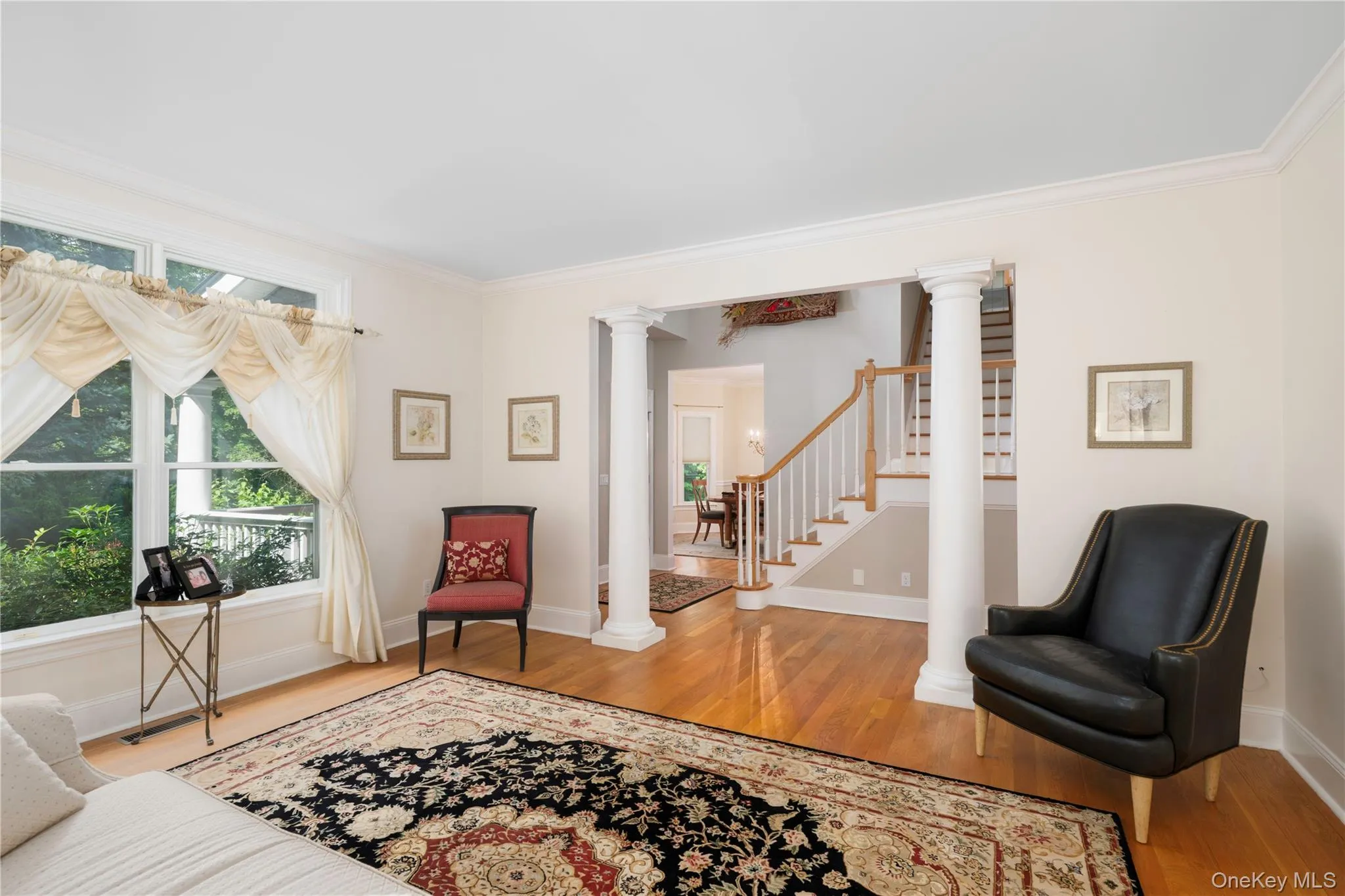 Bright interior space featuring wood-finish flooring, white trim, and architectural columns Bright interior space featuring wood-finish flooring, white trim, and architectural columns