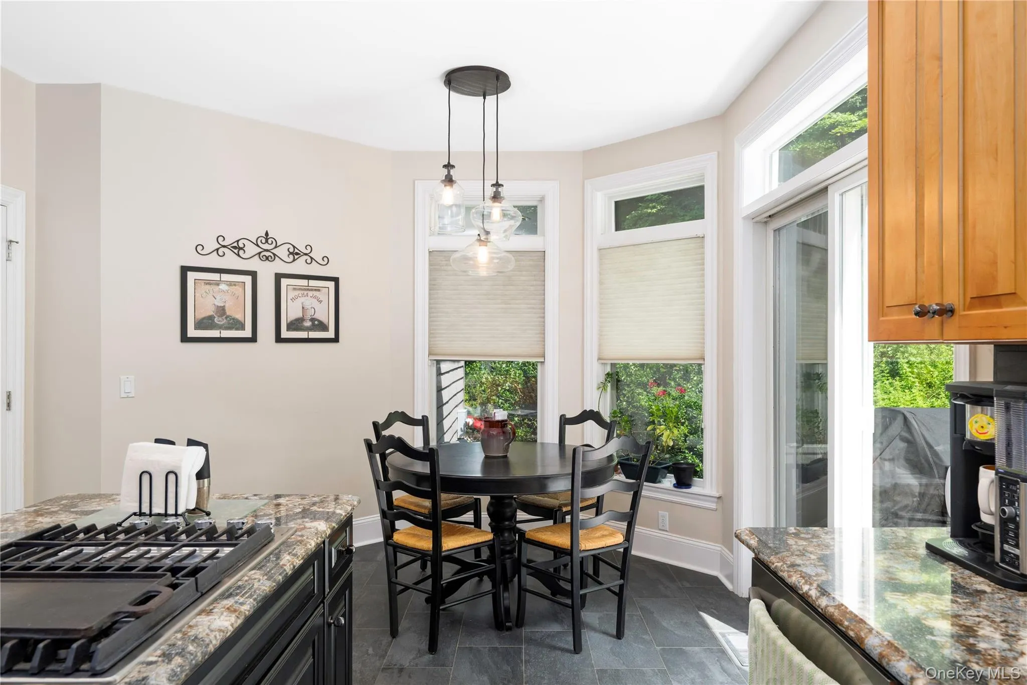 Bay window dining area with modern pendant lighting, slate-finish floor tiles, a sliding glass door, and adjacent kitchen counter with a built-in gas range Bay window dining area with modern pendant lighting, slate-finish floor tiles, a sliding glass door, and adjacent kitchen counter with a built-in gas range