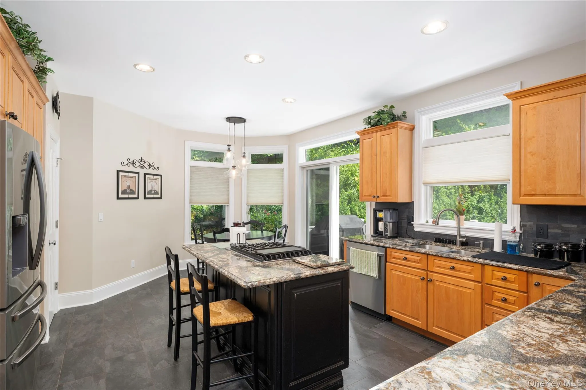 Kitchen featuring a central island with a gas range, recessed lighting, wood-finish cabinetry, gray stone countertops, and dark tile flooring Kitchen featuring a central island with a gas range, recessed lighting, wood-finish cabinetry, gray stone countertops, and dark tile flooring