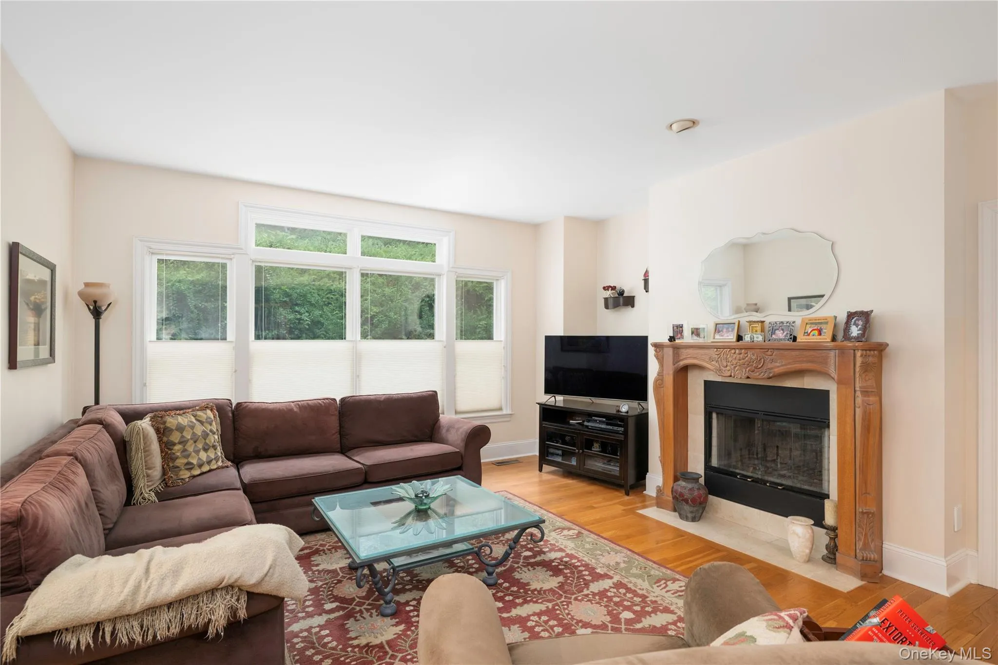 Living area featuring hardwood flooring, a decorative fireplace with an ornate wood mantel, and multiple windows Living area featuring hardwood flooring, a decorative fireplace with an ornate wood mantel, and multiple windows