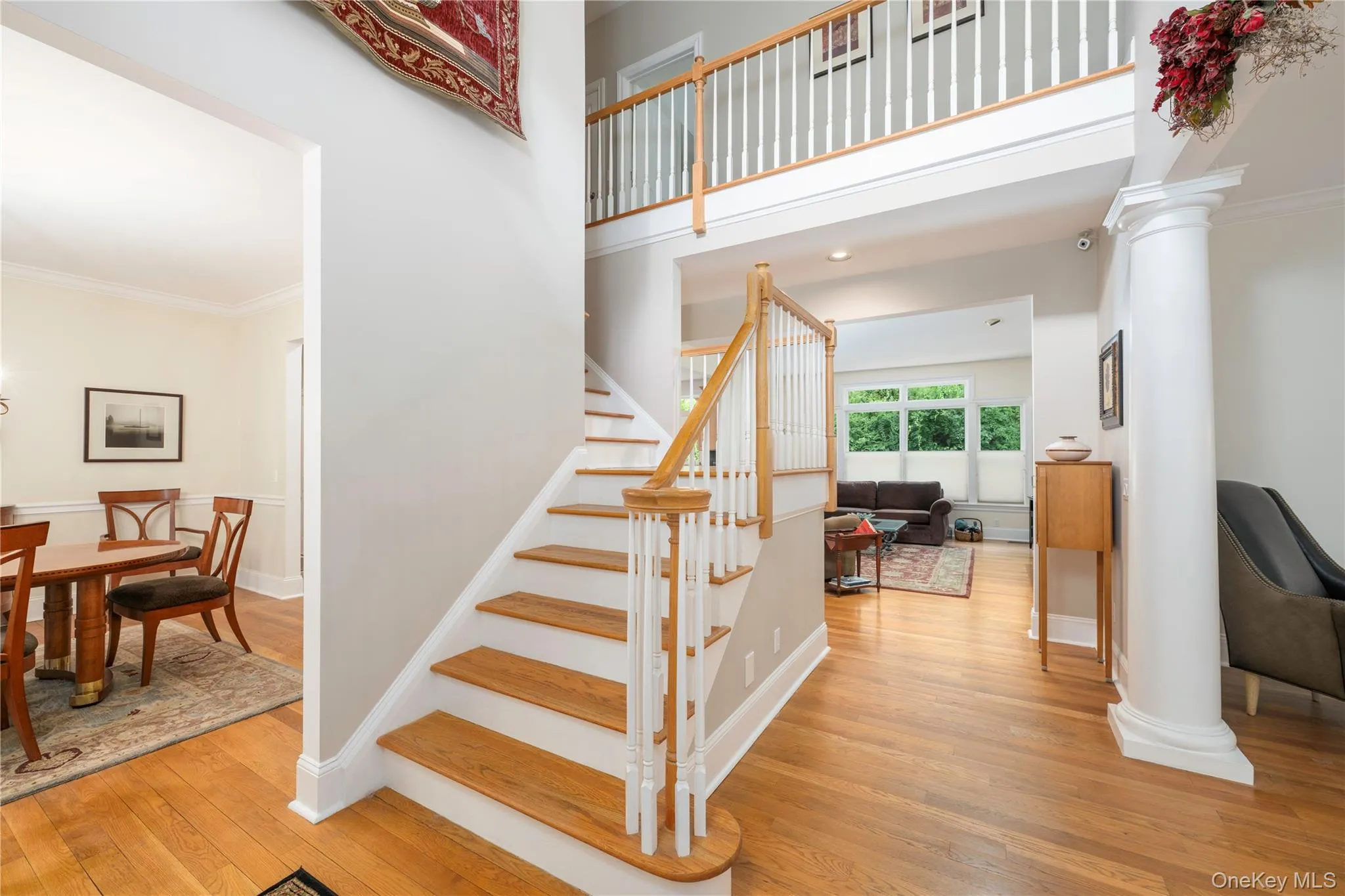 Two-story foyer featuring hardwood flooring, a prominent staircase with white risers and wood treads, a second-floor overlook, and a decorative column Two-story foyer featuring hardwood flooring, a prominent staircase with white risers and wood treads, a second-floor overlook, and a decorative column