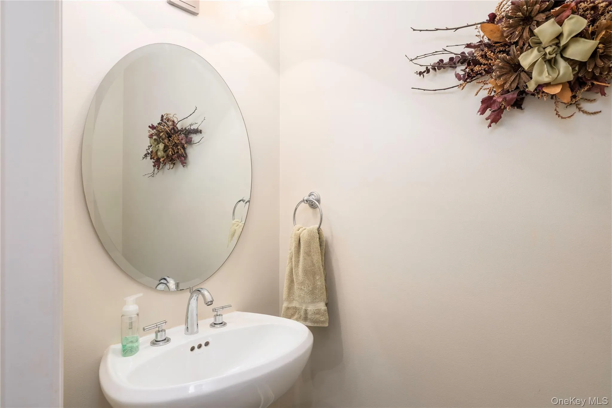Pedestal sink with chrome fixtures and an oval mirror, complemented by an overhead vanity light Pedestal sink with chrome fixtures and an oval mirror, complemented by an overhead vanity light