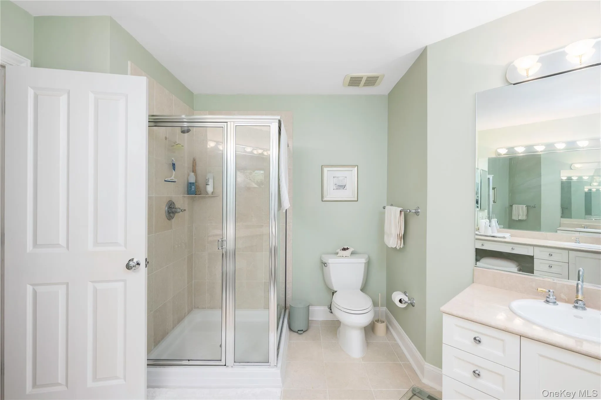 Bathroom with a glass-enclosed shower, a vanity featuring a single basin sink and light-colored countertop, and a white toilet Bathroom with a glass-enclosed shower, a vanity featuring a single basin sink and light-colored countertop, and a white toilet