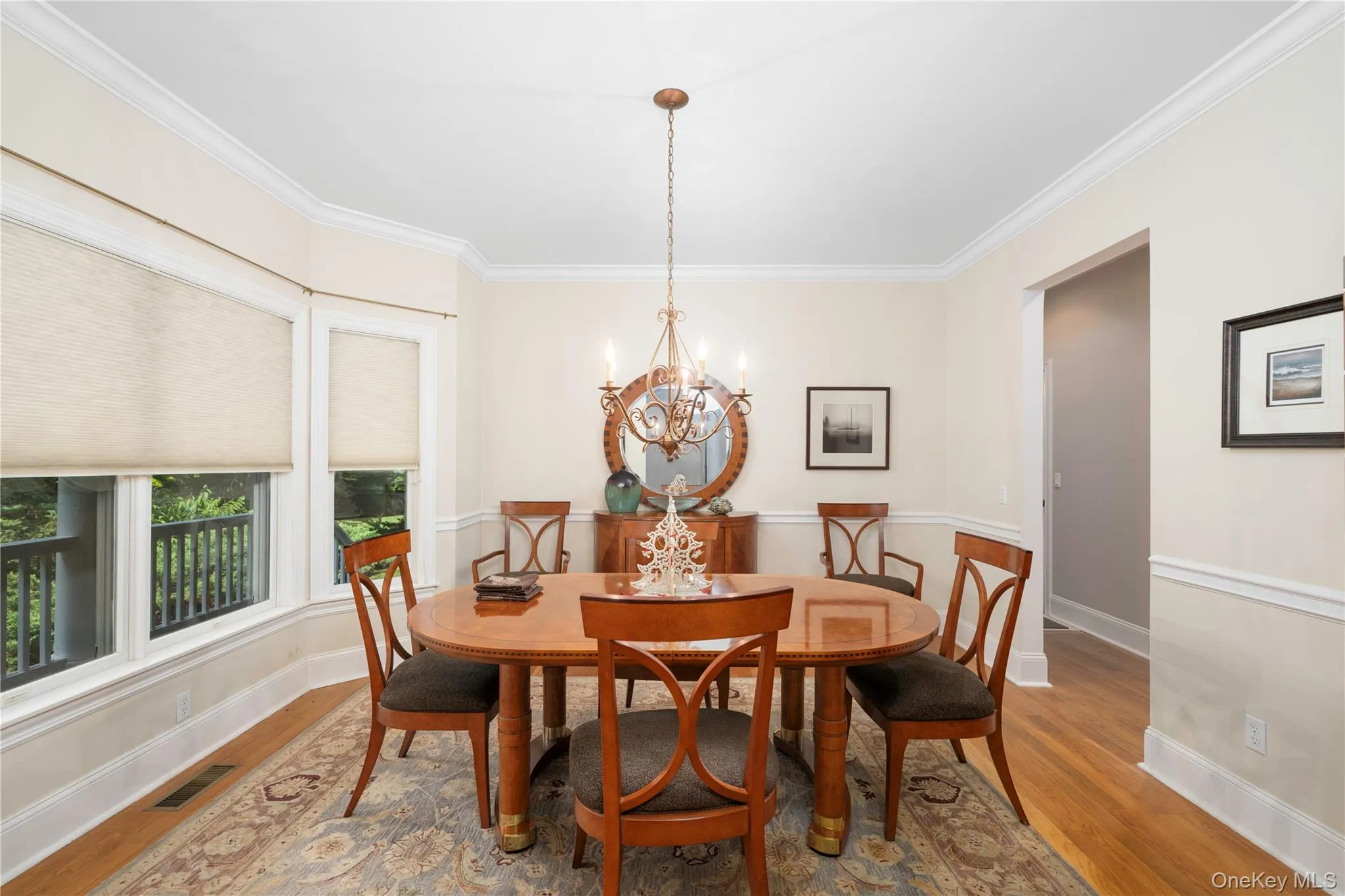 Formal dining area with wood-finish flooring, featuring a large bay window, crown molding, and wainscoting Formal dining area with wood-finish flooring, featuring a large bay window, crown molding, and wainscoting