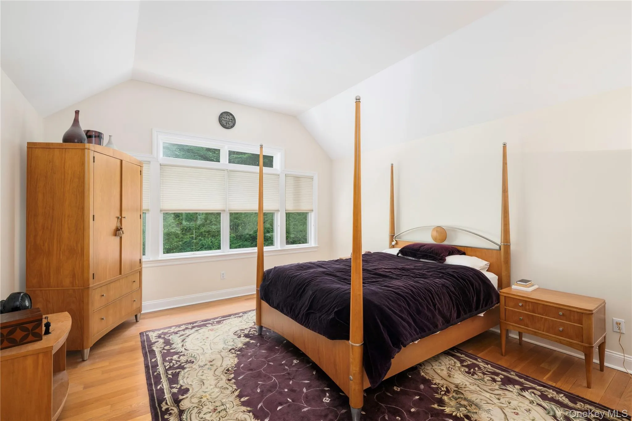 Vaulted ceiling bedroom featuring hardwood flooring, a large multi-pane window, and neutral wall tones Vaulted ceiling bedroom featuring hardwood flooring, a large multi-pane window, and neutral wall tones