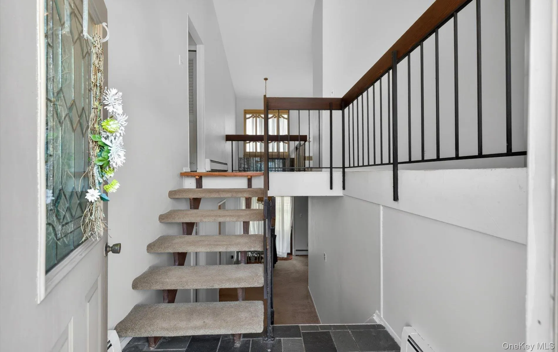 Entryway featuring slate tile flooring, a multi-level staircase with carpeted treads and open risers, and a wrought iron and wood-finish railing system Entryway featuring slate tile flooring, a multi-level staircase with carpeted treads and open risers, and a wrought iron and wood-finish railing system