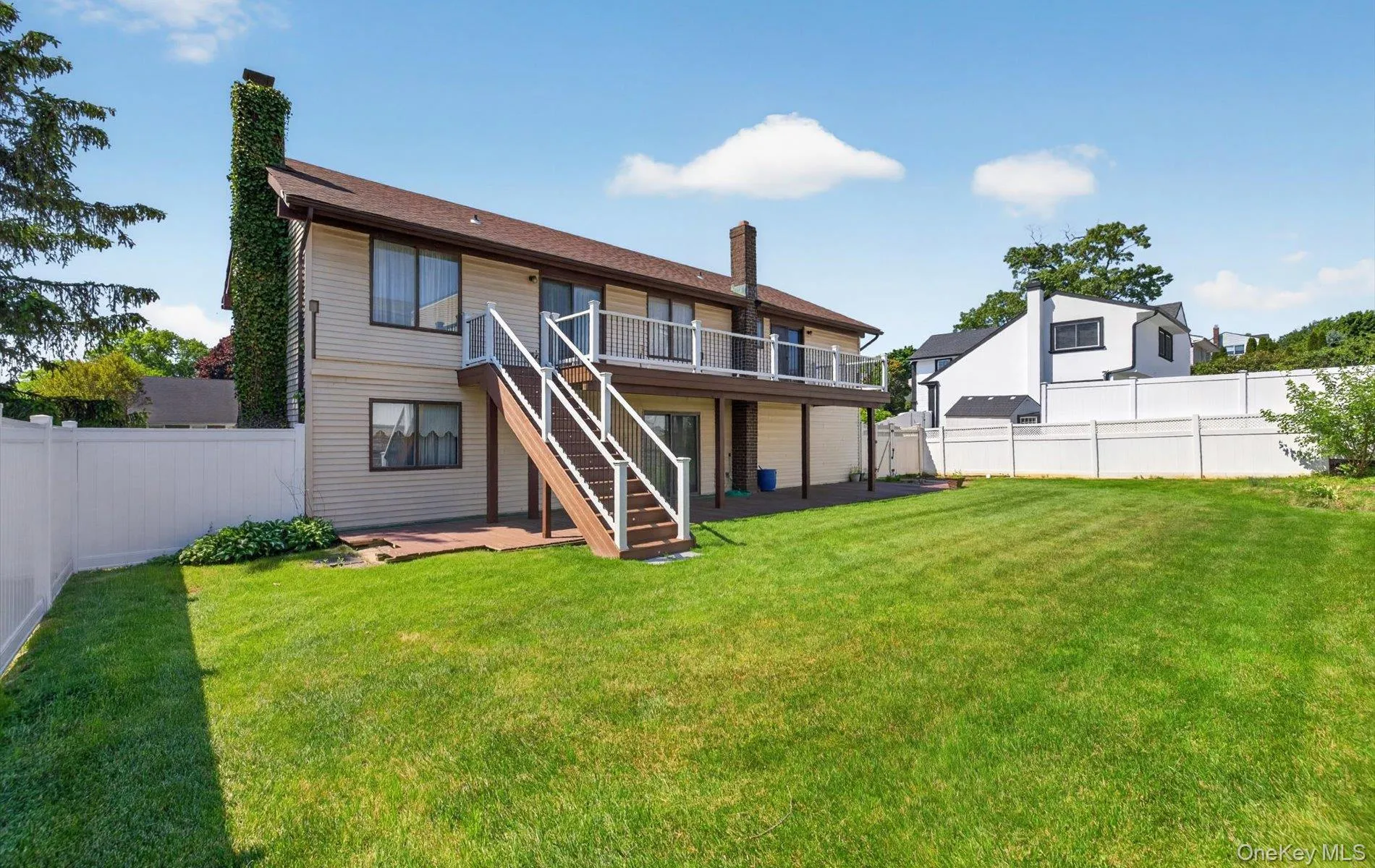 Expansive rear yard featuring a large green lawn, a multi-level wooden deck, and a white vinyl fence Expansive rear yard featuring a large green lawn, a multi-level wooden deck, and a white vinyl fence