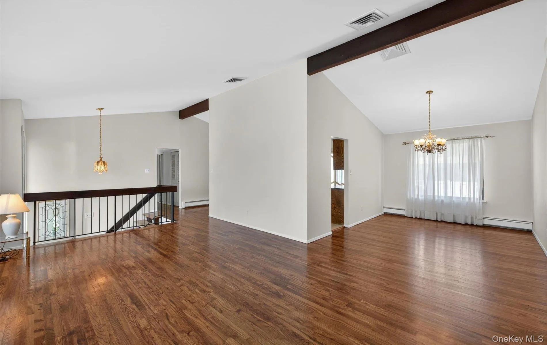 Spacious interior featuring wood-finish flooring throughout, an open-concept layout, vaulted ceiling, and exposed ceiling beams Spacious interior featuring wood-finish flooring throughout, an open-concept layout, vaulted ceiling, and exposed ceiling beams
