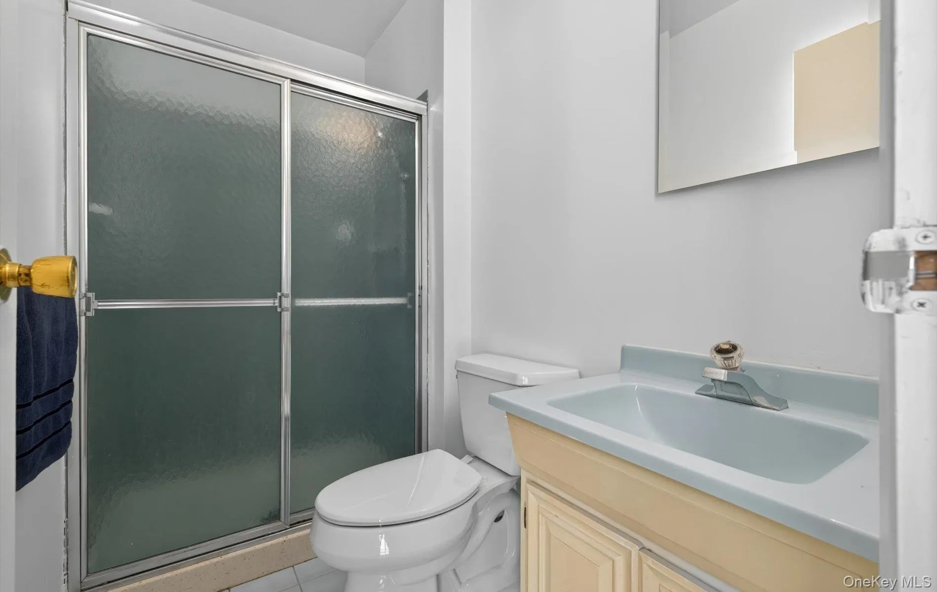 Bathroom featuring a shower with frosted glass sliding doors, a light blue vanity sink, and a wall-mounted mirror Bathroom featuring a shower with frosted glass sliding doors, a light blue vanity sink, and a wall-mounted mirror