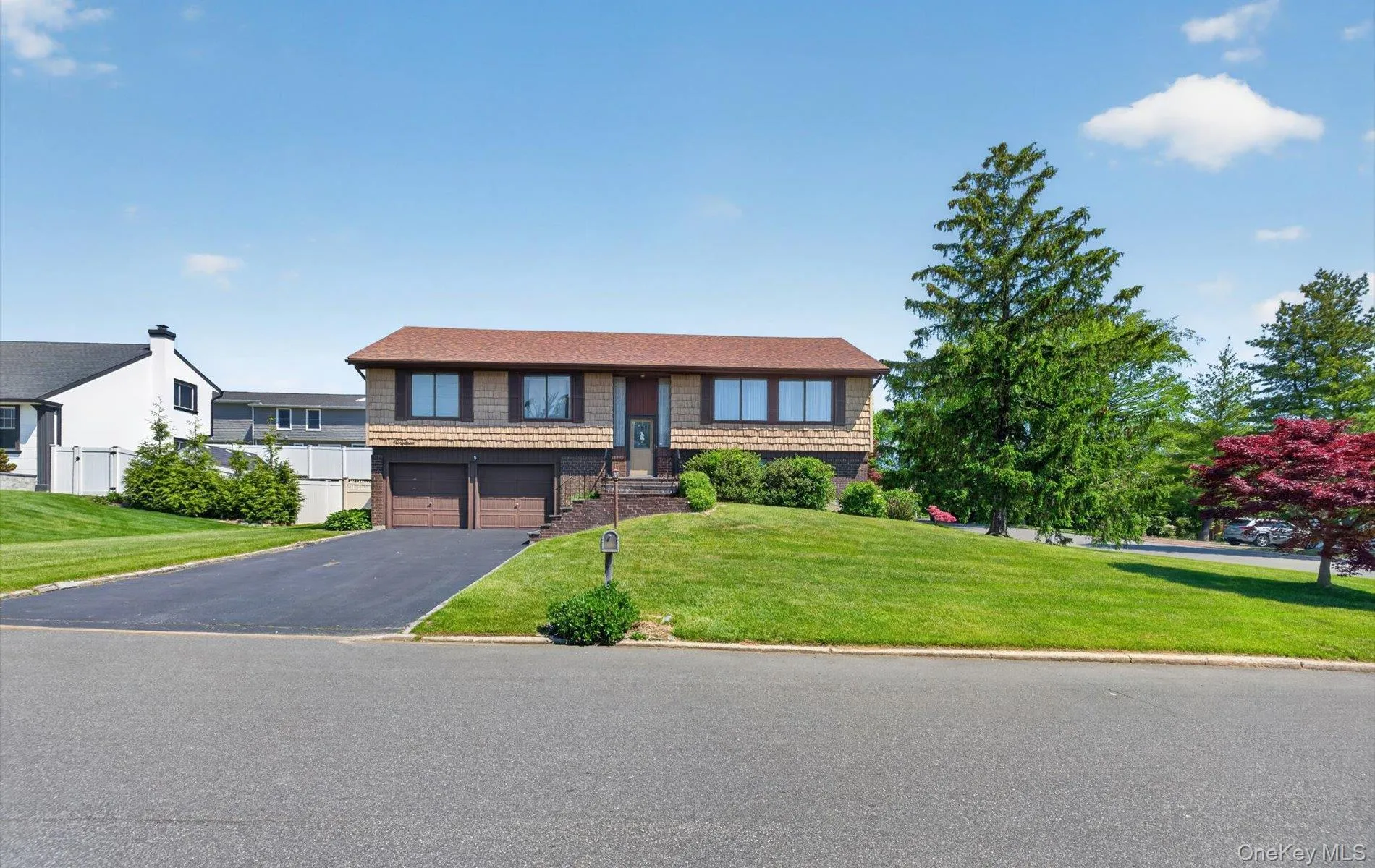 Split-level residence featuring a two-car garage with individual doors, a paved driveway, and a shingle roof Split-level residence featuring a two-car garage with individual doors, a paved driveway, and a shingle roof