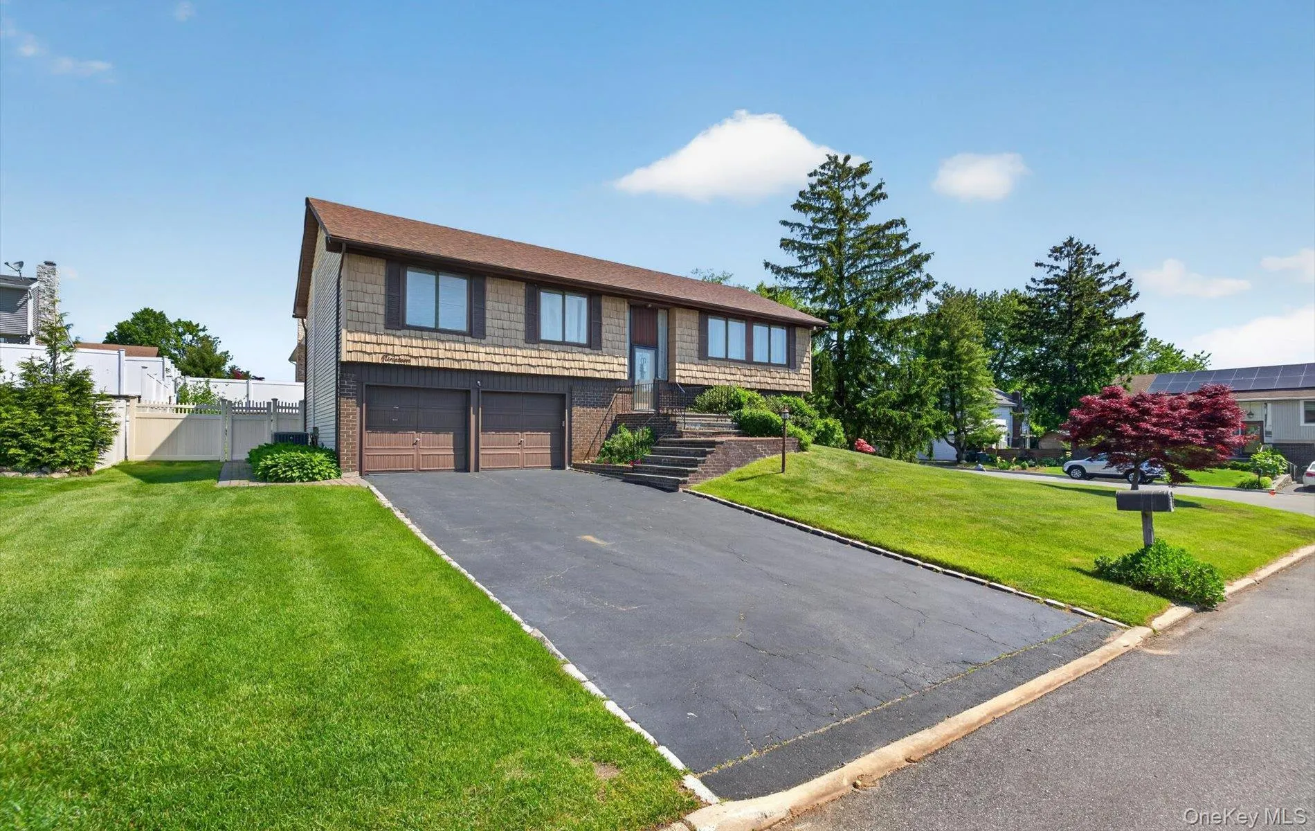 Split-level residence featuring a two-car garage, shingle and brick exterior, and a paved driveway Split-level residence featuring a two-car garage, shingle and brick exterior, and a paved driveway