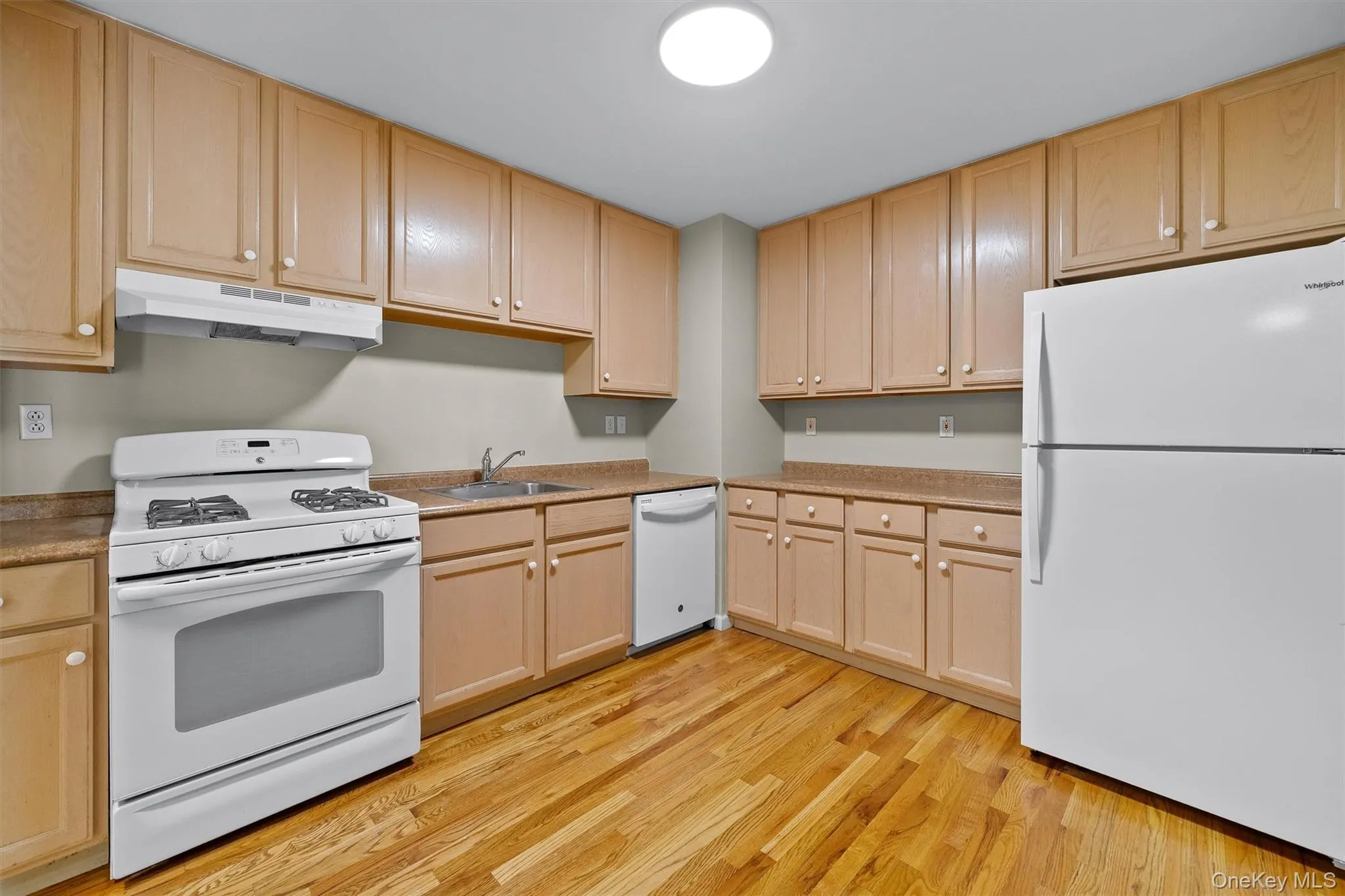 Kitchen featuring light brown cabinetry, white appliances, under cabinet range hood, and a sink Kitchen featuring light brown cabinetry, white appliances, under cabinet range hood, and a sink
