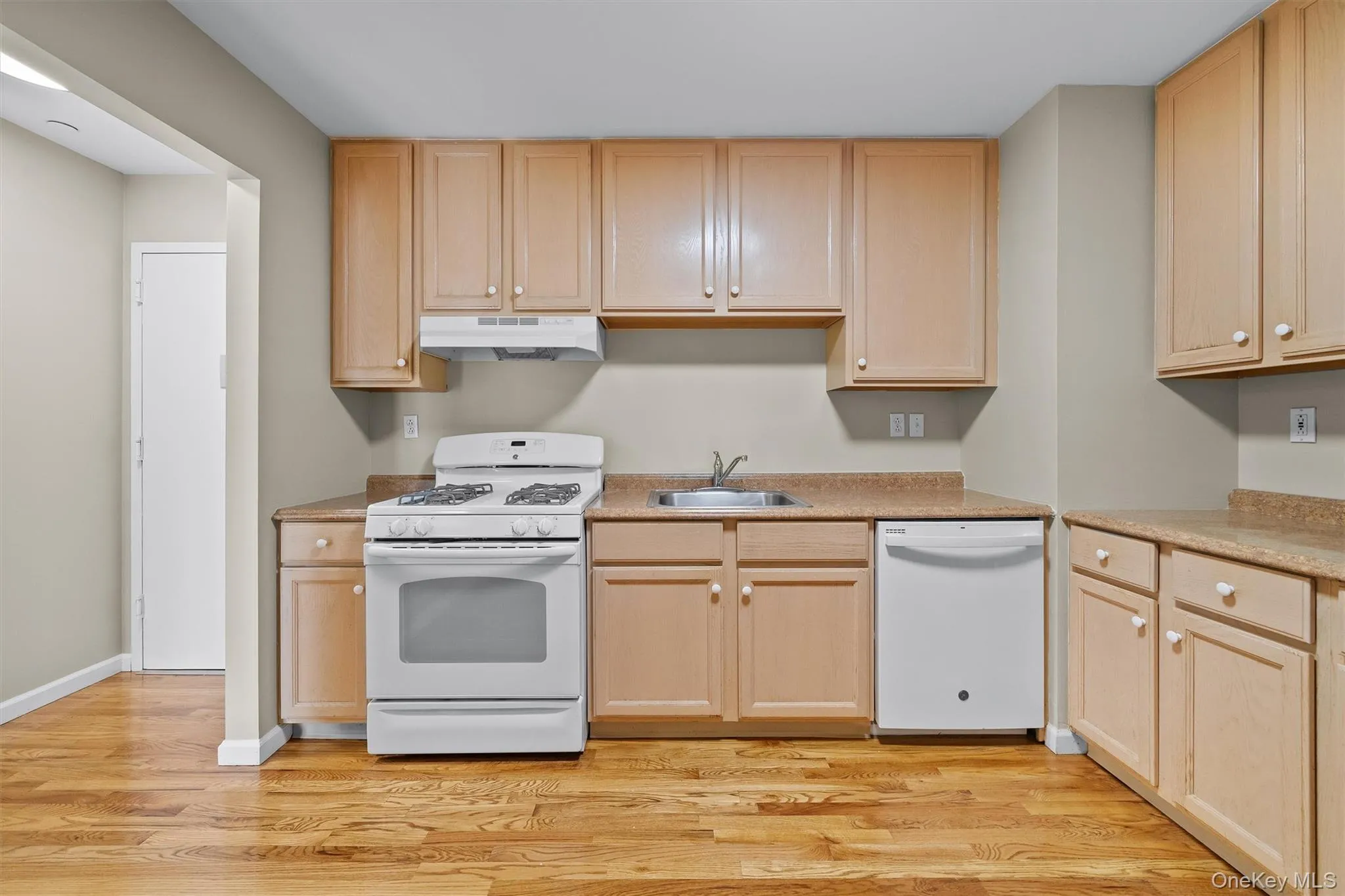 Kitchen with white appliances, light brown cabinetry, under cabinet range hood, light wood finished floors, and a sink Kitchen with white appliances, light brown cabinetry, under cabinet range hood, light wood finished floors, and a sink