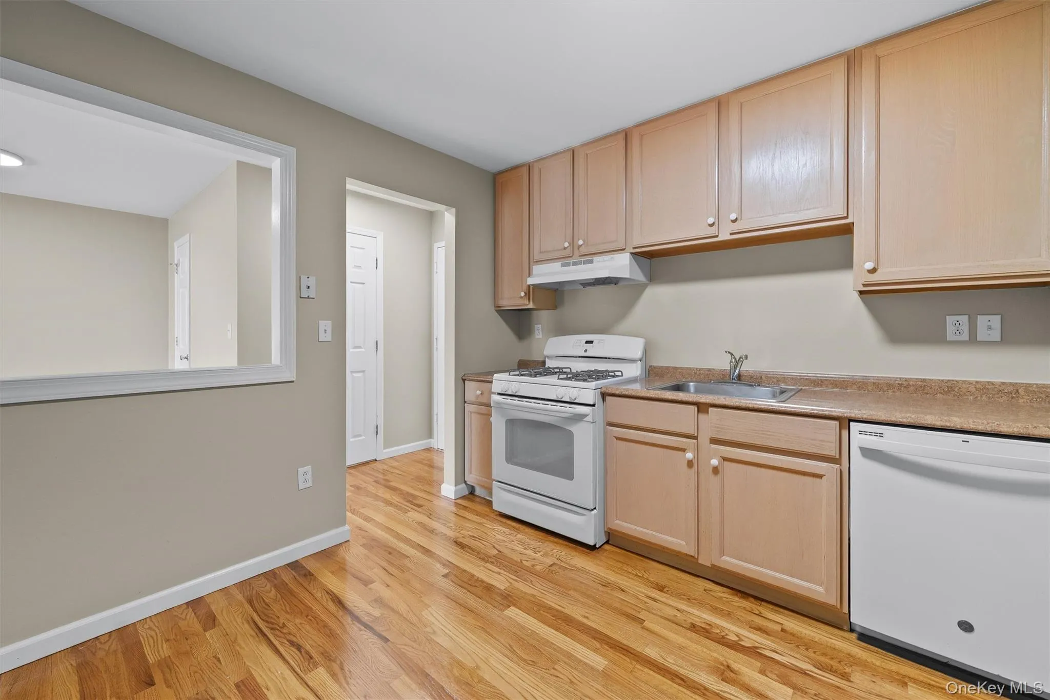 Kitchen with light wood finished floors, a sink, under cabinet range hood, light brown cabinetry, and white appliances Kitchen with light wood finished floors, a sink, under cabinet range hood, light brown cabinetry, and white appliances