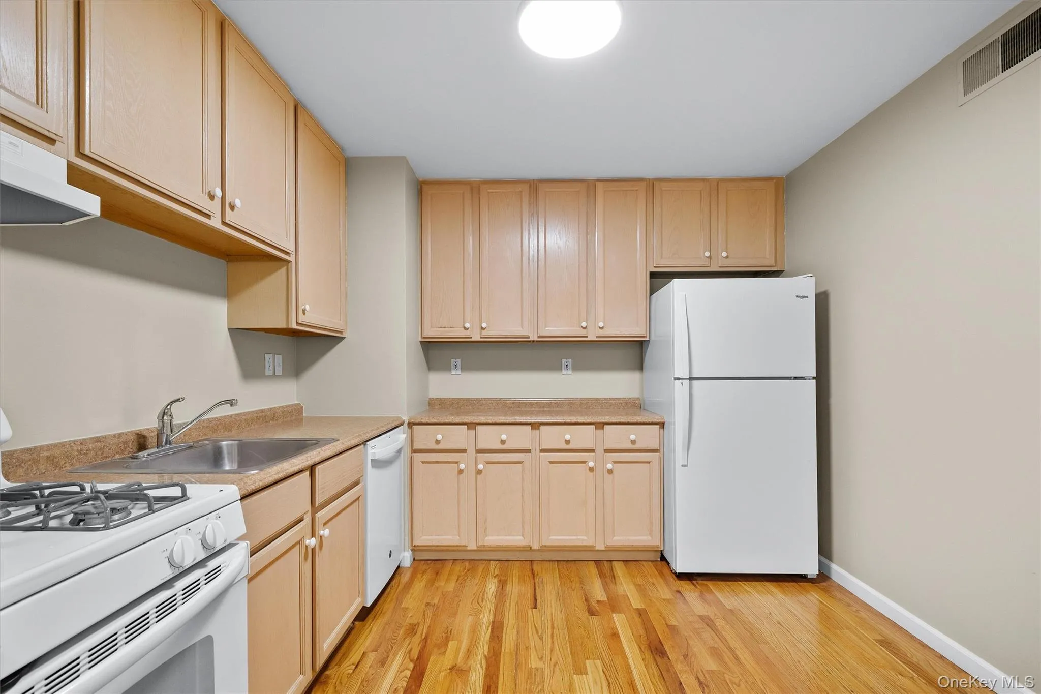 Kitchen with visible vents, white appliances, light wood-style floors, and light countertops Kitchen with visible vents, white appliances, light wood-style floors, and light countertops