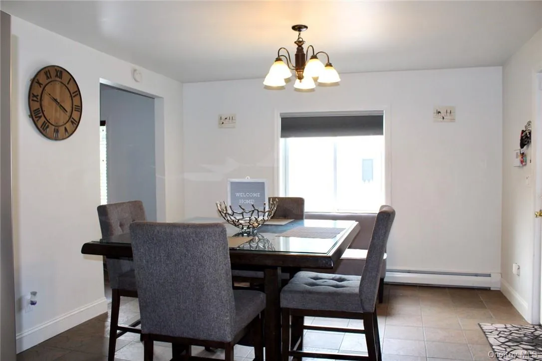 Dining room with an inviting chandelier, dark tile patterned flooring, and a baseboard heating unit Dining room with an inviting chandelier, dark tile patterned flooring, and a baseboard heating unit