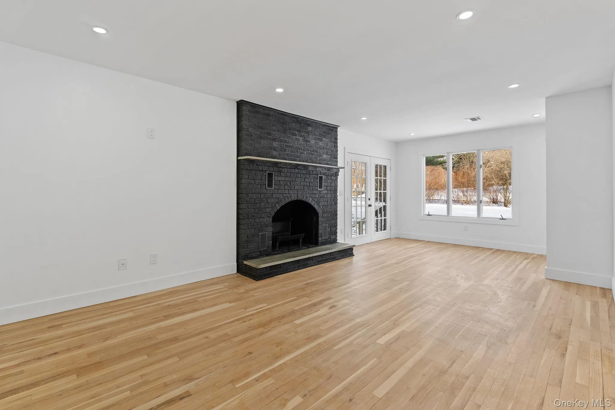 Unfurnished living room with light wood finished floors, french doors, a fireplace, and recessed lighting Unfurnished living room with light wood finished floors, french doors, a fireplace, and recessed lighting