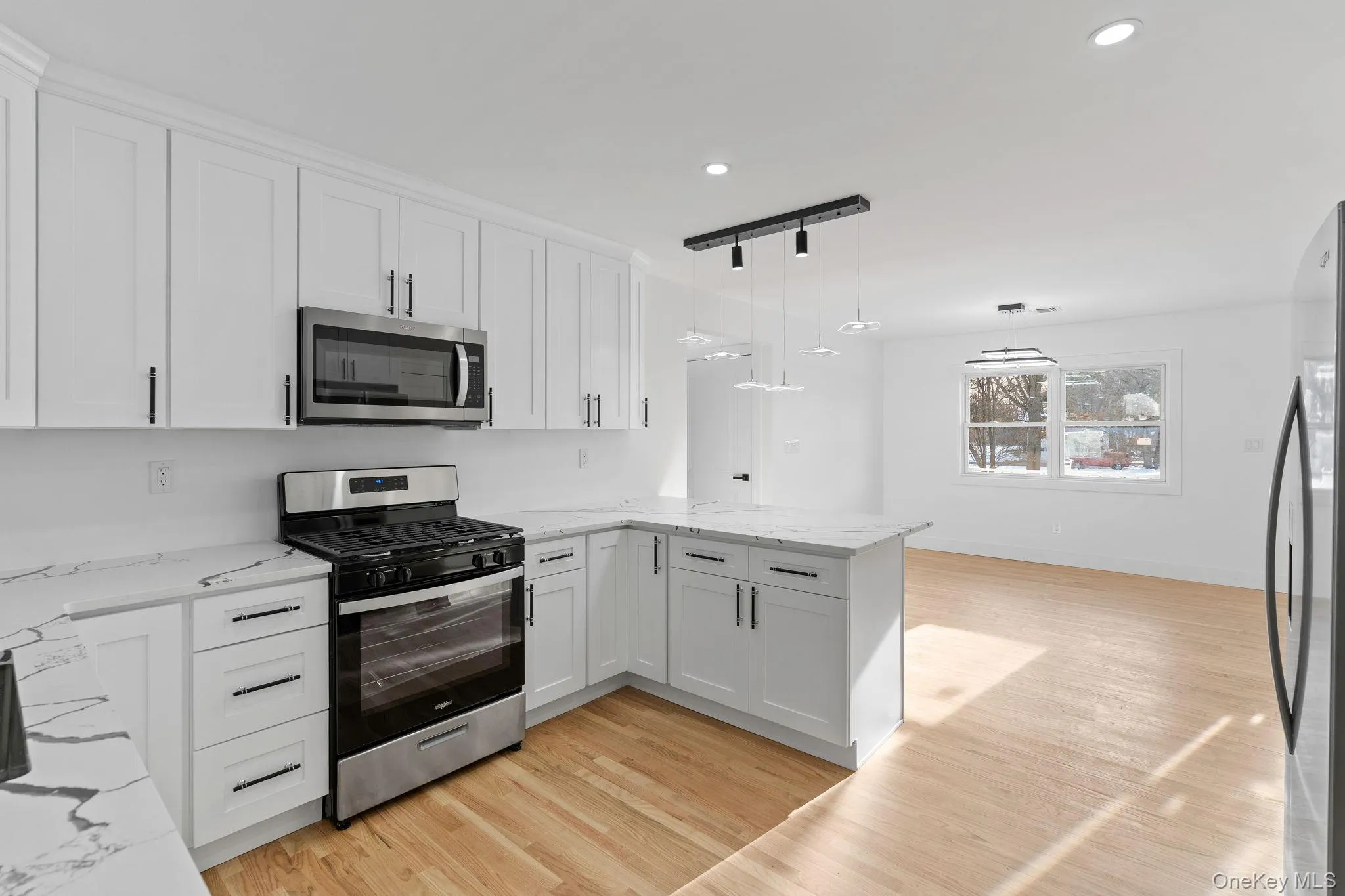 Kitchen featuring stainless steel appliances, decorative light fixtures, white cabinetry, light stone countertops, and light wood-type flooring Kitchen featuring stainless steel appliances, decorative light fixtures, white cabinetry, light stone countertops, and light wood-type flooring
