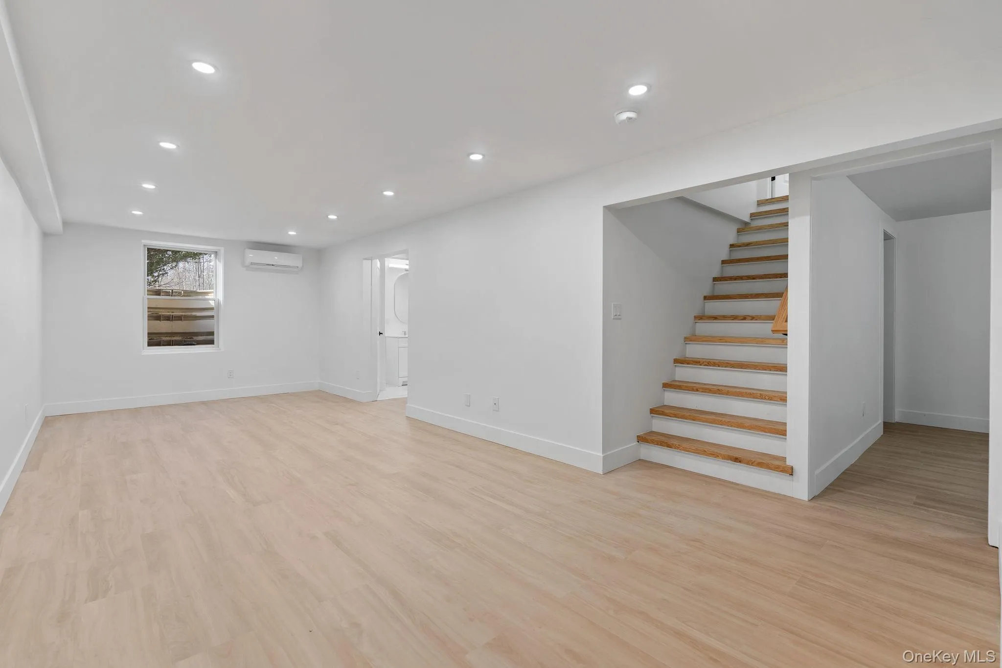 Below grade area with recessed lighting, light wood-style flooring, stairs, and a wall unit AC Below grade area with recessed lighting, light wood-style flooring, stairs, and a wall unit AC