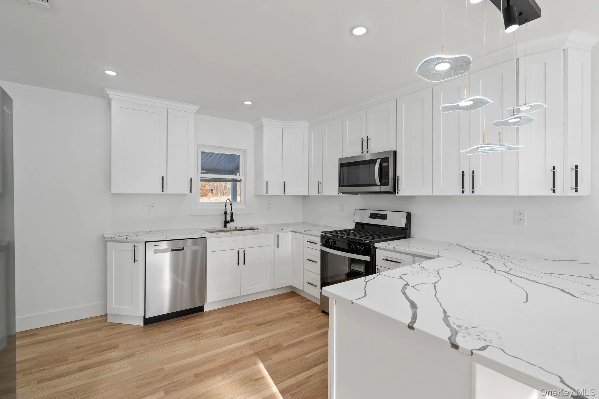 Kitchen featuring appliances with stainless steel finishes, light stone countertops, white cabinets, decorative light fixtures, and light wood-style flooring Kitchen featuring appliances with stainless steel finishes, light stone countertops, white cabinets, decorative light fixtures, and light wood-style flooring