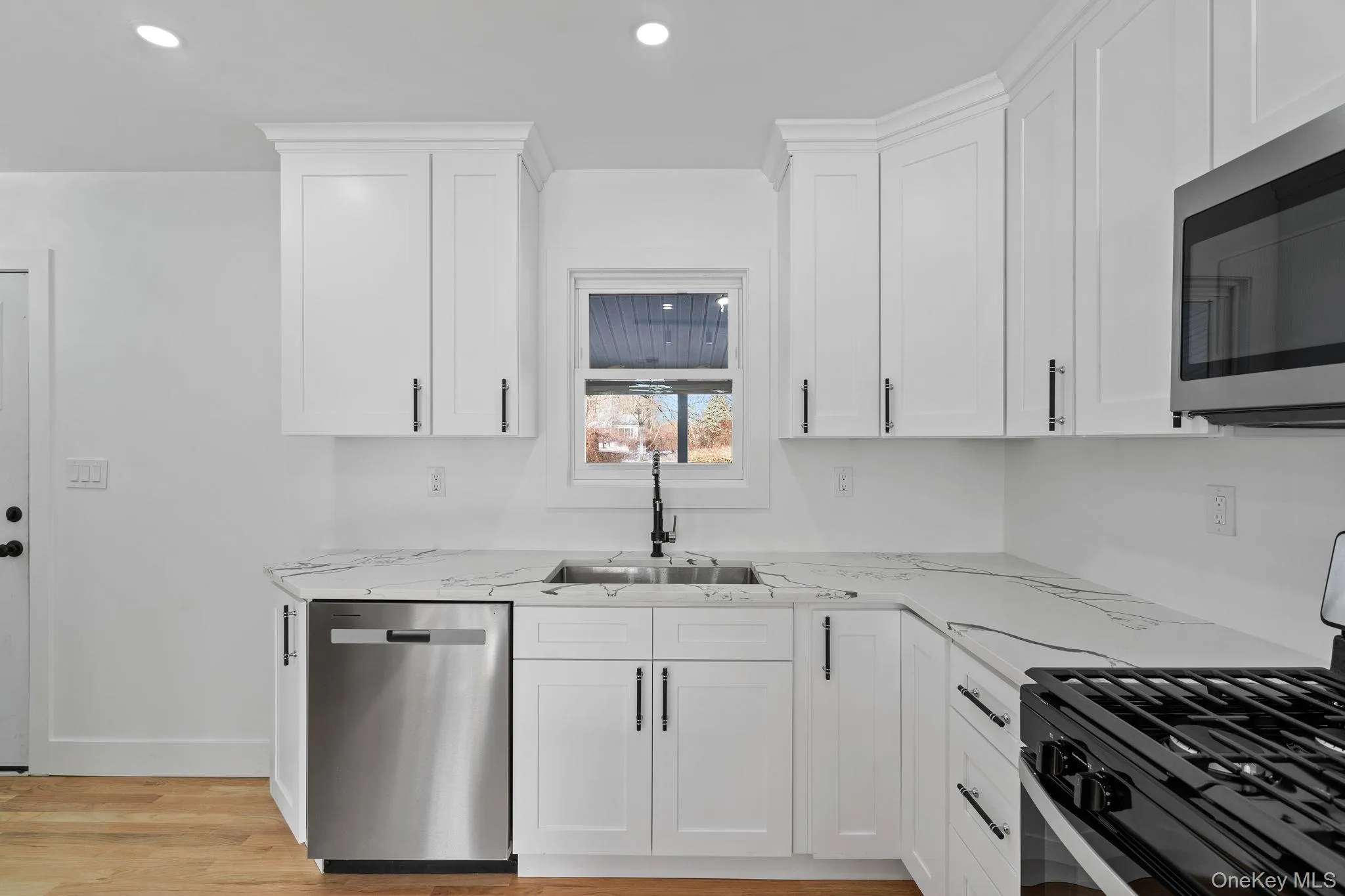 Kitchen with appliances with stainless steel finishes, white cabinets, light wood-style flooring, recessed lighting, and light stone countertops Kitchen with appliances with stainless steel finishes, white cabinets, light wood-style flooring, recessed lighting, and light stone countertops