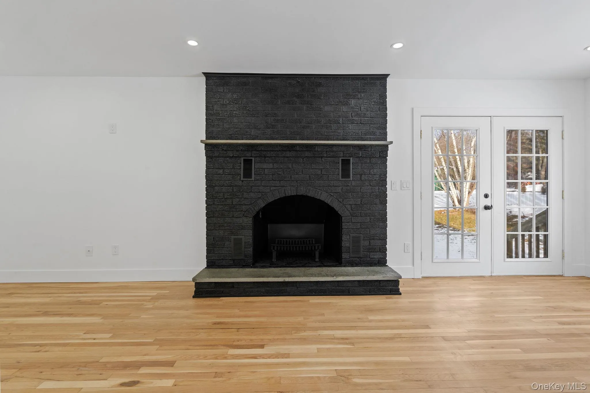 Unfurnished living room featuring light wood finished floors, recessed lighting, a brick fireplace, and french doors Unfurnished living room featuring light wood finished floors, recessed lighting, a brick fireplace, and french doors