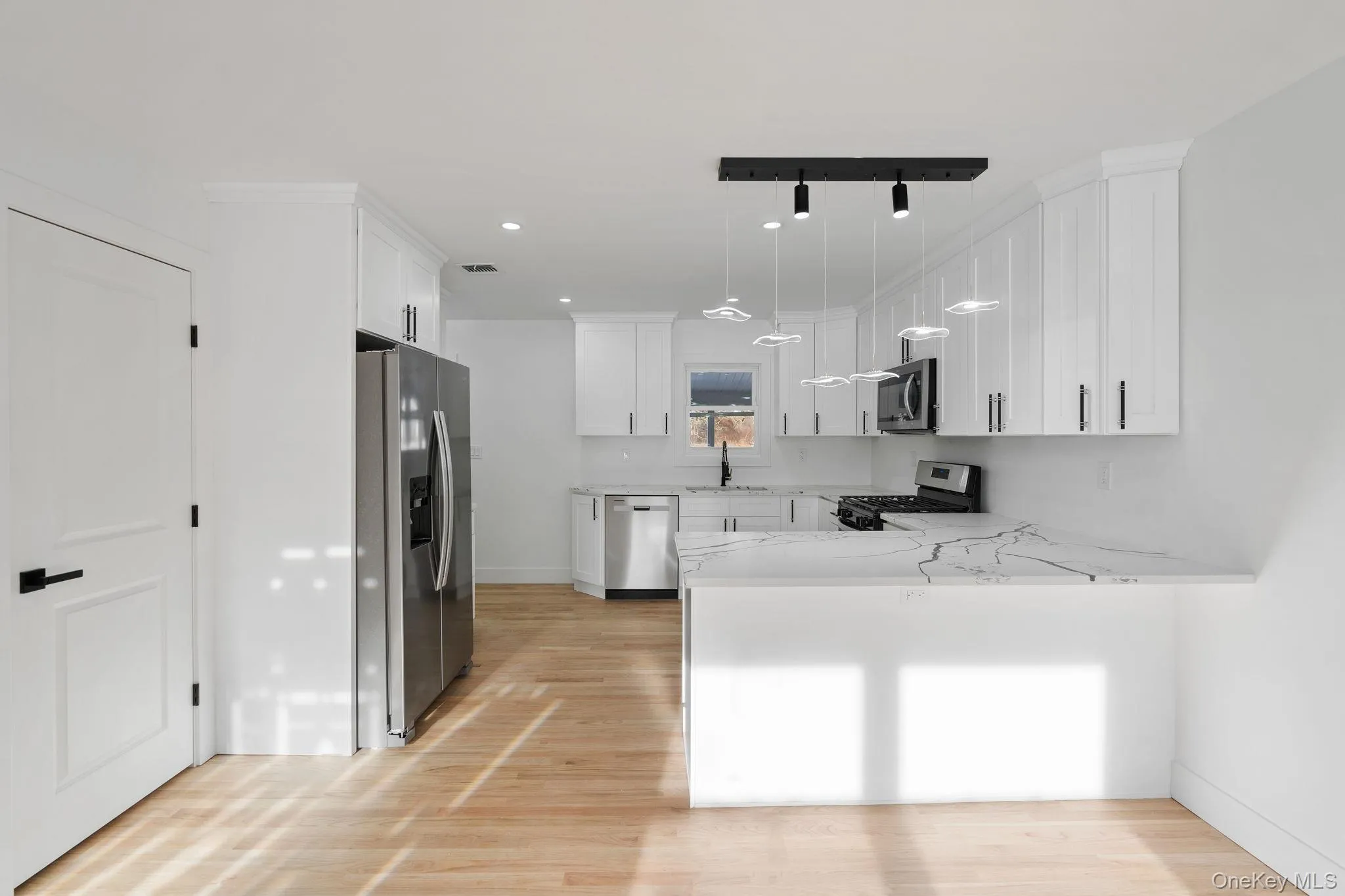 Kitchen with white cabinets, stainless steel appliances, decorative light fixtures, light stone countertops, and a peninsula Kitchen with white cabinets, stainless steel appliances, decorative light fixtures, light stone countertops, and a peninsula