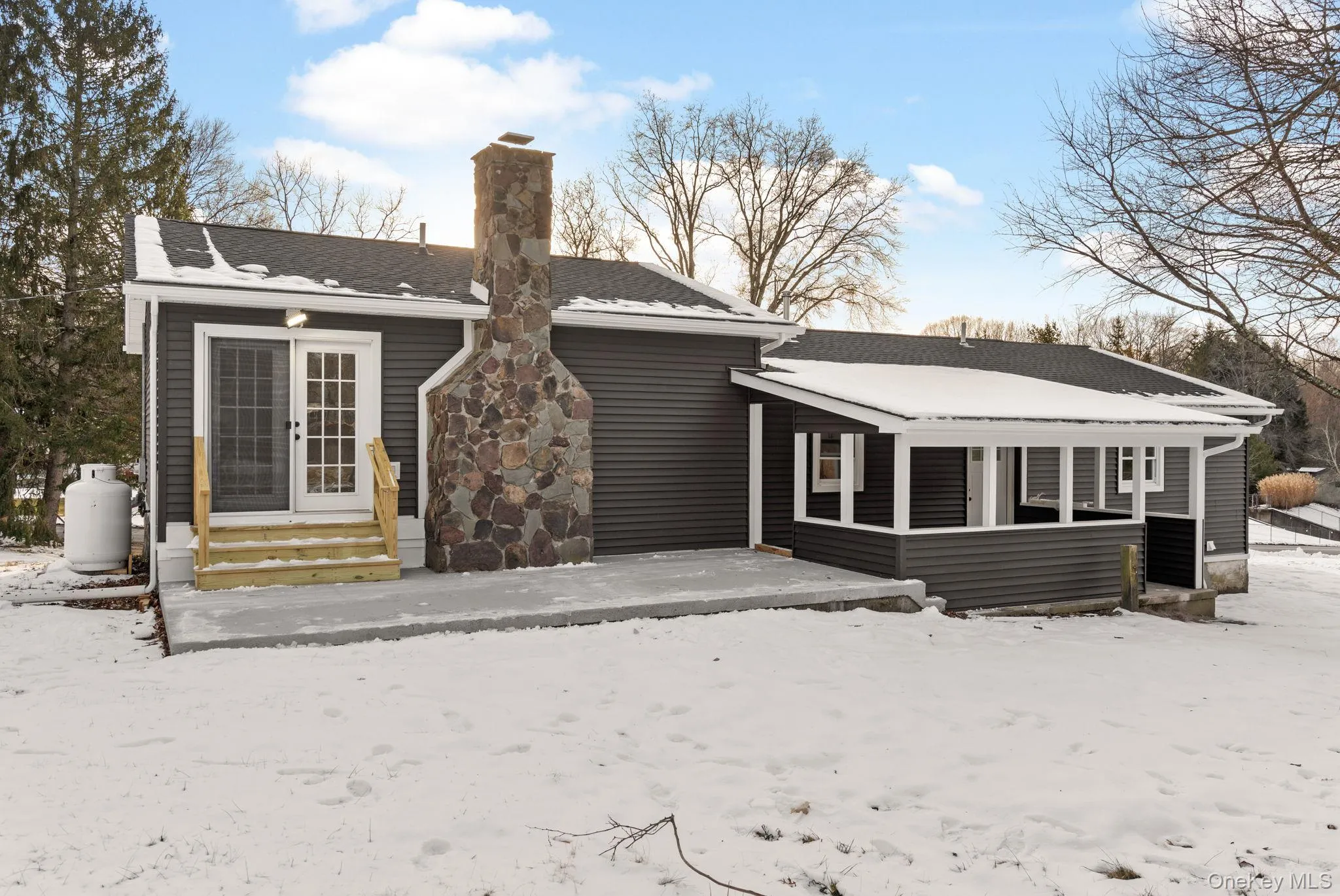 Snow covered back of property featuring a patio area, entry steps, a chimney, and roof with shingles Snow covered back of property featuring a patio area, entry steps, a chimney, and roof with shingles