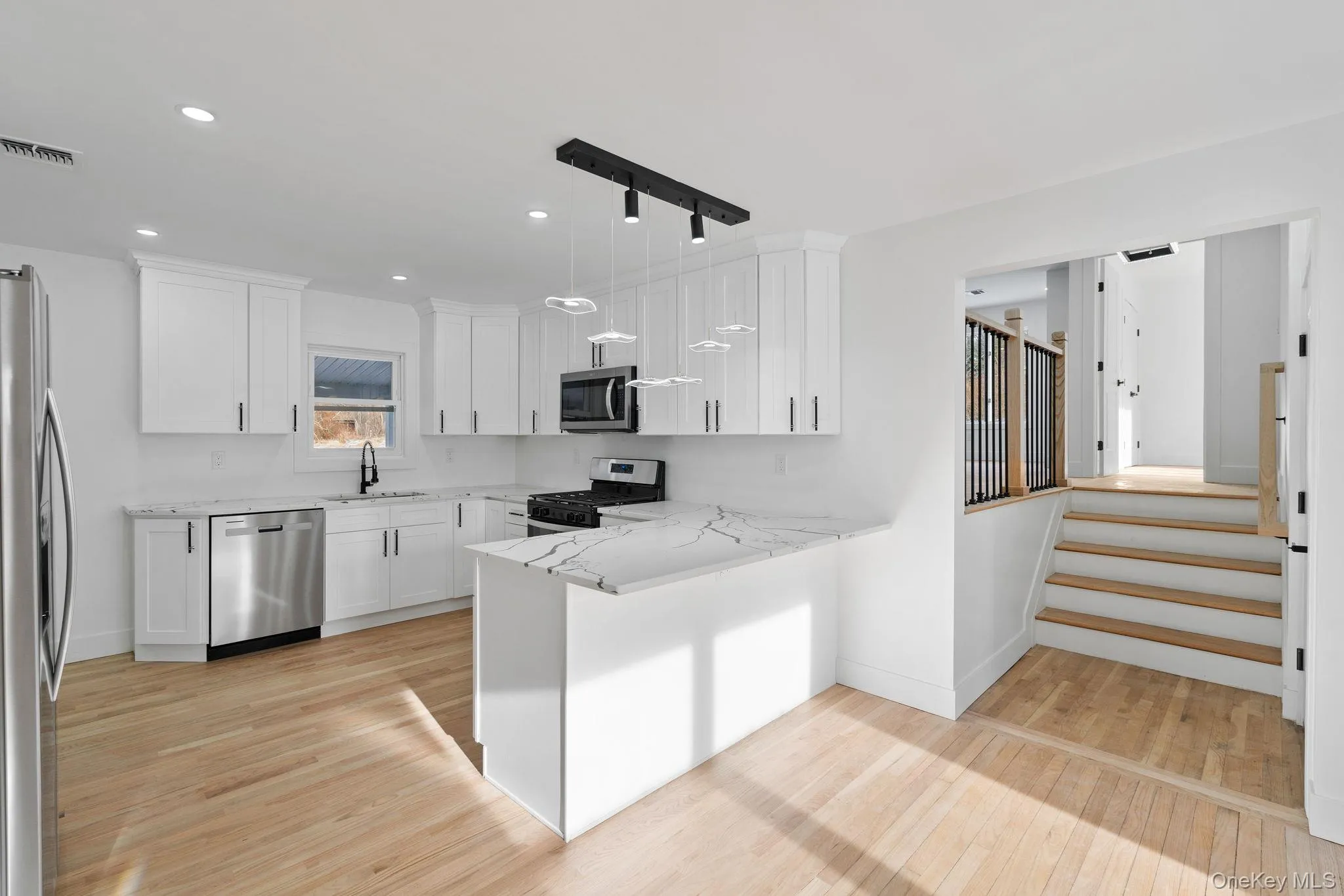 Kitchen featuring appliances with stainless steel finishes, white cabinets, a peninsula, decorative light fixtures, and light wood-type flooring Kitchen featuring appliances with stainless steel finishes, white cabinets, a peninsula, decorative light fixtures, and light wood-type flooring