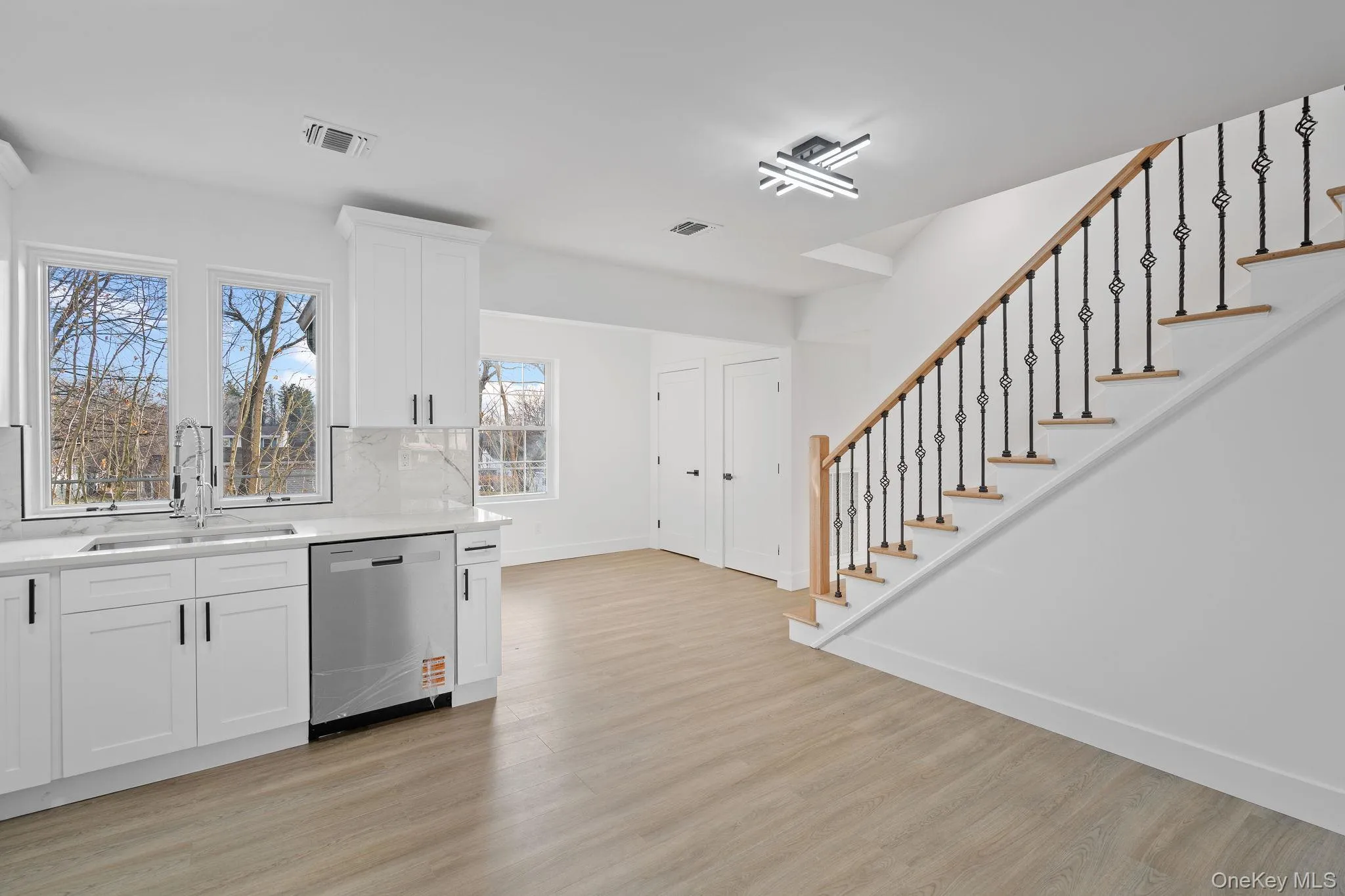 Kitchen with white cabinetry, dishwasher, light wood-style floors, and backsplash Kitchen with white cabinetry, dishwasher, light wood-style floors, and backsplash