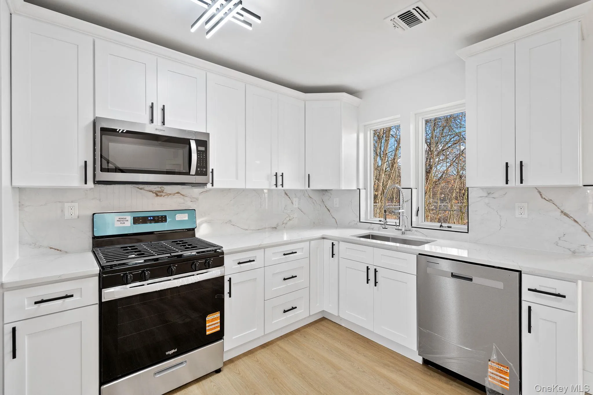 Kitchen featuring appliances with stainless steel finishes, light stone counters, white cabinetry, and backsplash Kitchen featuring appliances with stainless steel finishes, light stone counters, white cabinetry, and backsplash