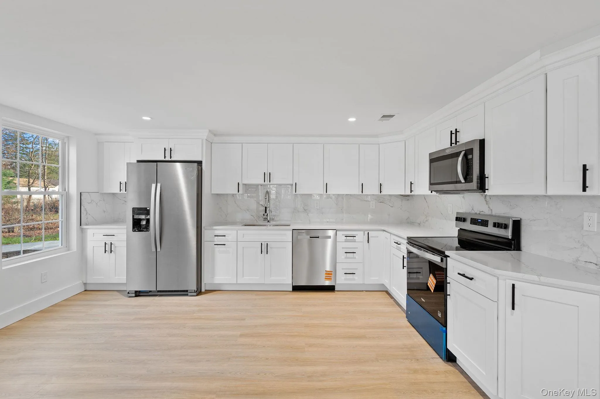 Kitchen with stainless steel appliances, white cabinets, light wood-style flooring, and tasteful backsplash Kitchen with stainless steel appliances, white cabinets, light wood-style flooring, and tasteful backsplash