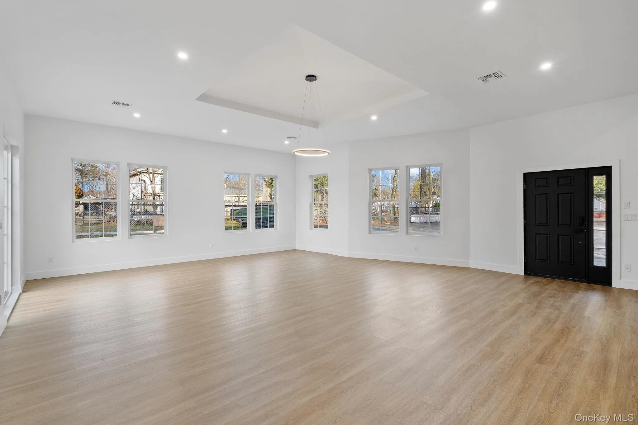 Unfurnished living room with recessed lighting, light wood finished floors, and a raised ceiling Unfurnished living room with recessed lighting, light wood finished floors, and a raised ceiling
