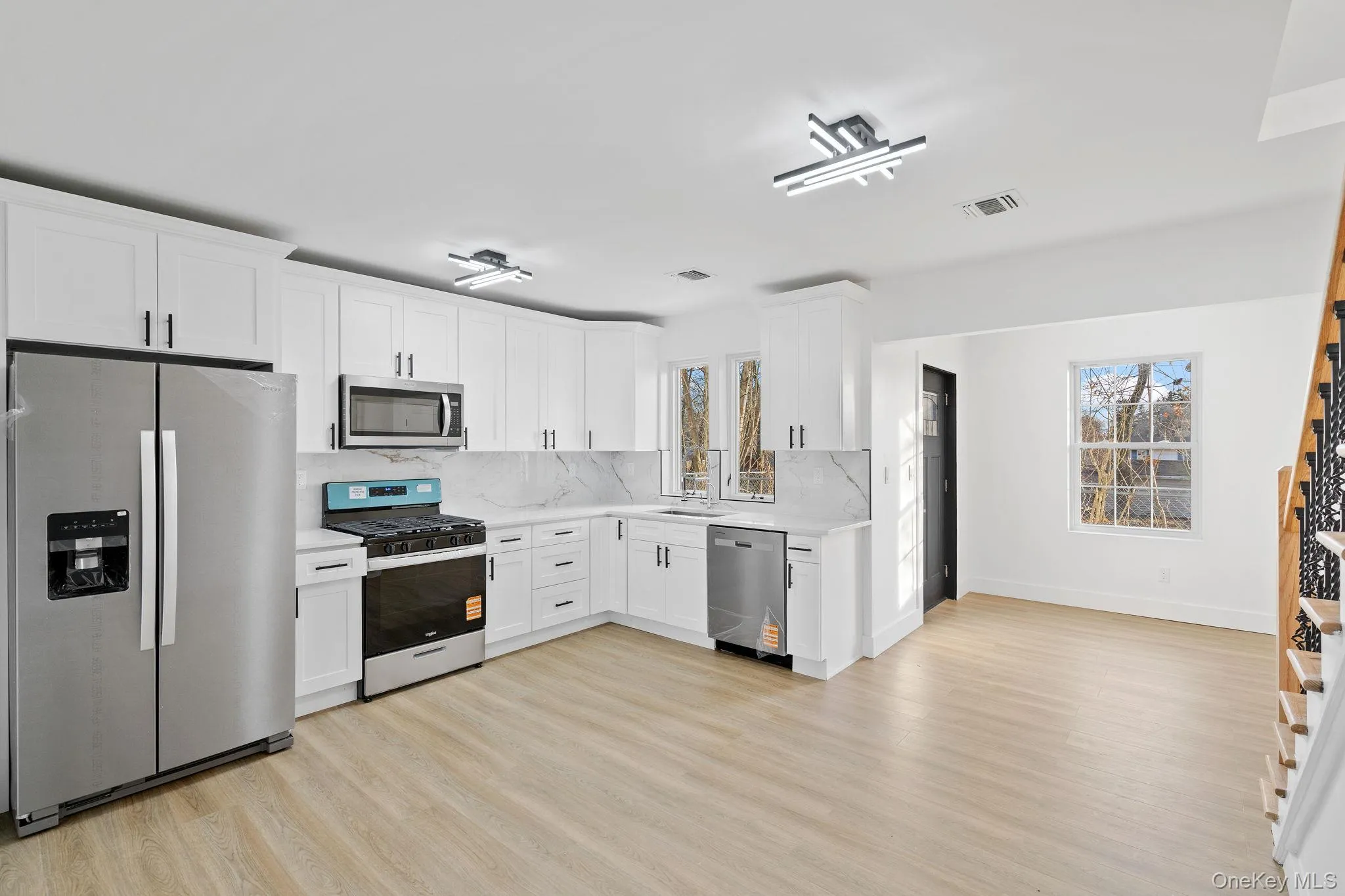 Kitchen with stainless steel appliances, white cabinets, light wood-style floors, decorative backsplash, and light stone countertops Kitchen with stainless steel appliances, white cabinets, light wood-style floors, decorative backsplash, and light stone countertops