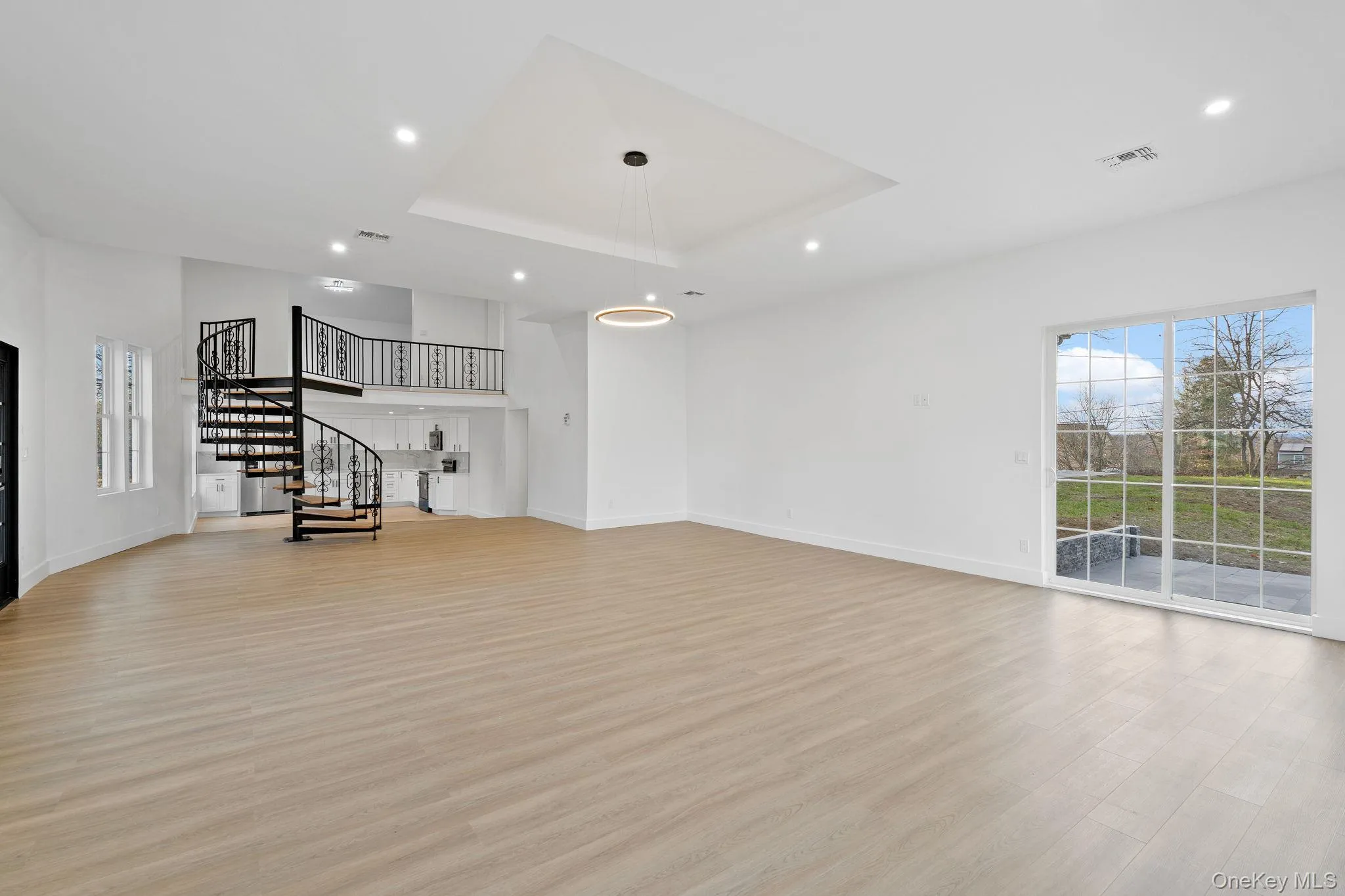 Unfurnished living room with healthy amount of natural light, recessed lighting, light wood-style flooring, stairs, and a tray ceiling Unfurnished living room with healthy amount of natural light, recessed lighting, light wood-style flooring, stairs, and a tray ceiling