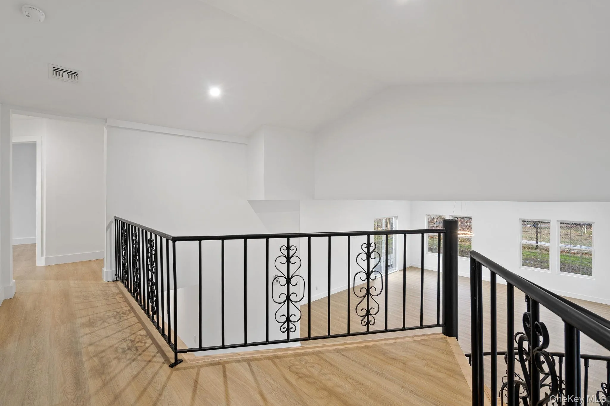 Corridor with an upstairs landing, light wood finished floors, lofted ceiling, and recessed lighting Corridor with an upstairs landing, light wood finished floors, lofted ceiling, and recessed lighting