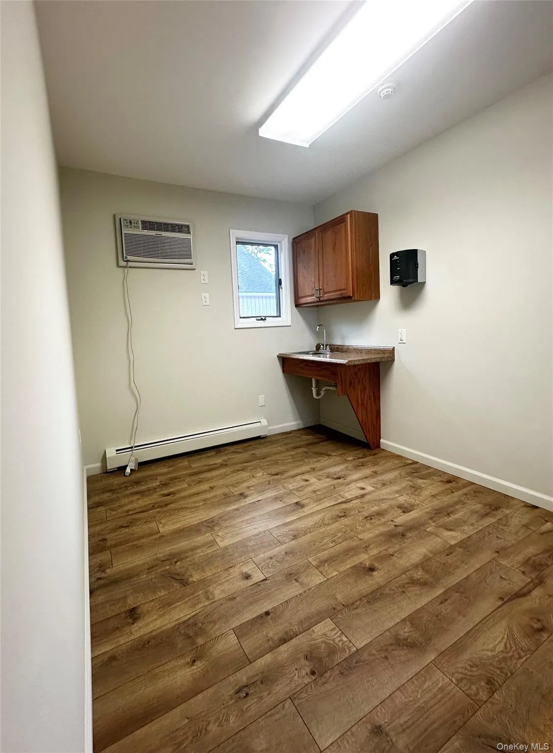 Washroom with dark wood-style floors, a baseboard radiator, and a wall unit AC Washroom with dark wood-style floors, a baseboard radiator, and a wall unit AC