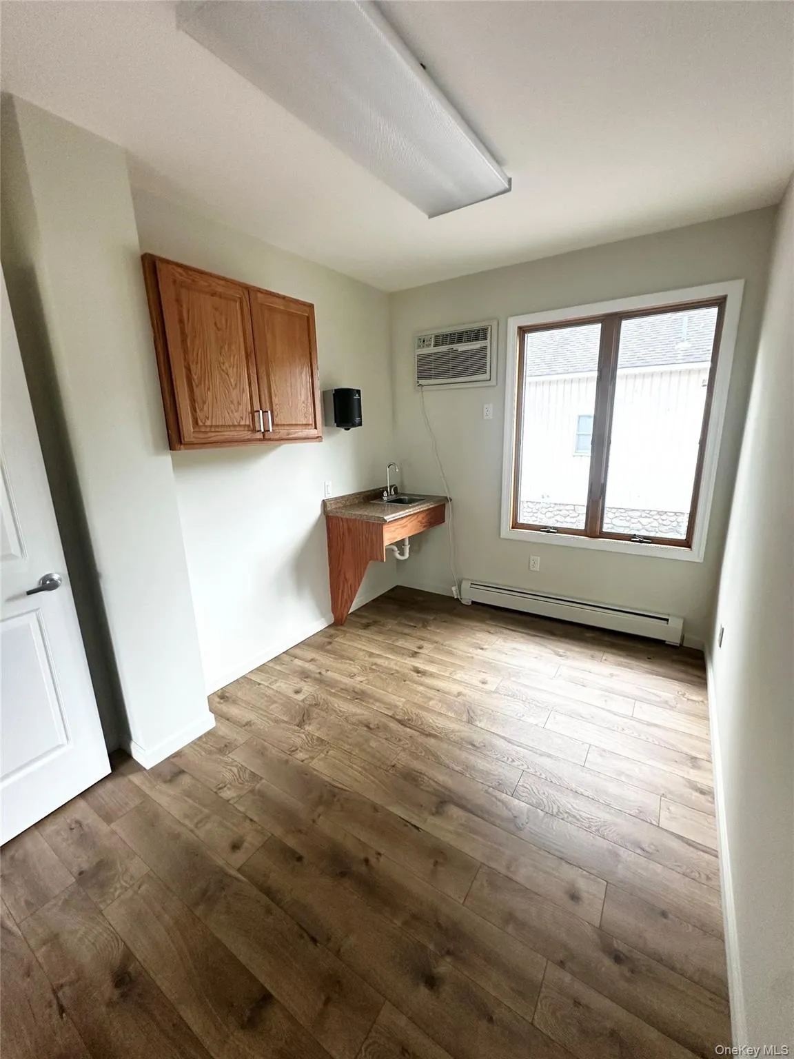 Laundry room featuring a baseboard heating unit, light wood-style flooring, and a wall mounted air conditioner Laundry room featuring a baseboard heating unit, light wood-style flooring, and a wall mounted air conditioner