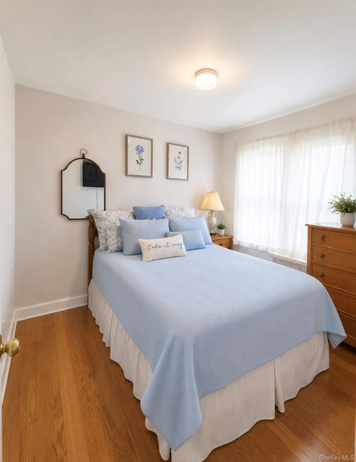 Bedroom featuring wood-finish flooring, a flush-mount ceiling light fixture, and a window with sheer curtains Bedroom featuring wood-finish flooring, a flush-mount ceiling light fixture, and a window with sheer curtains